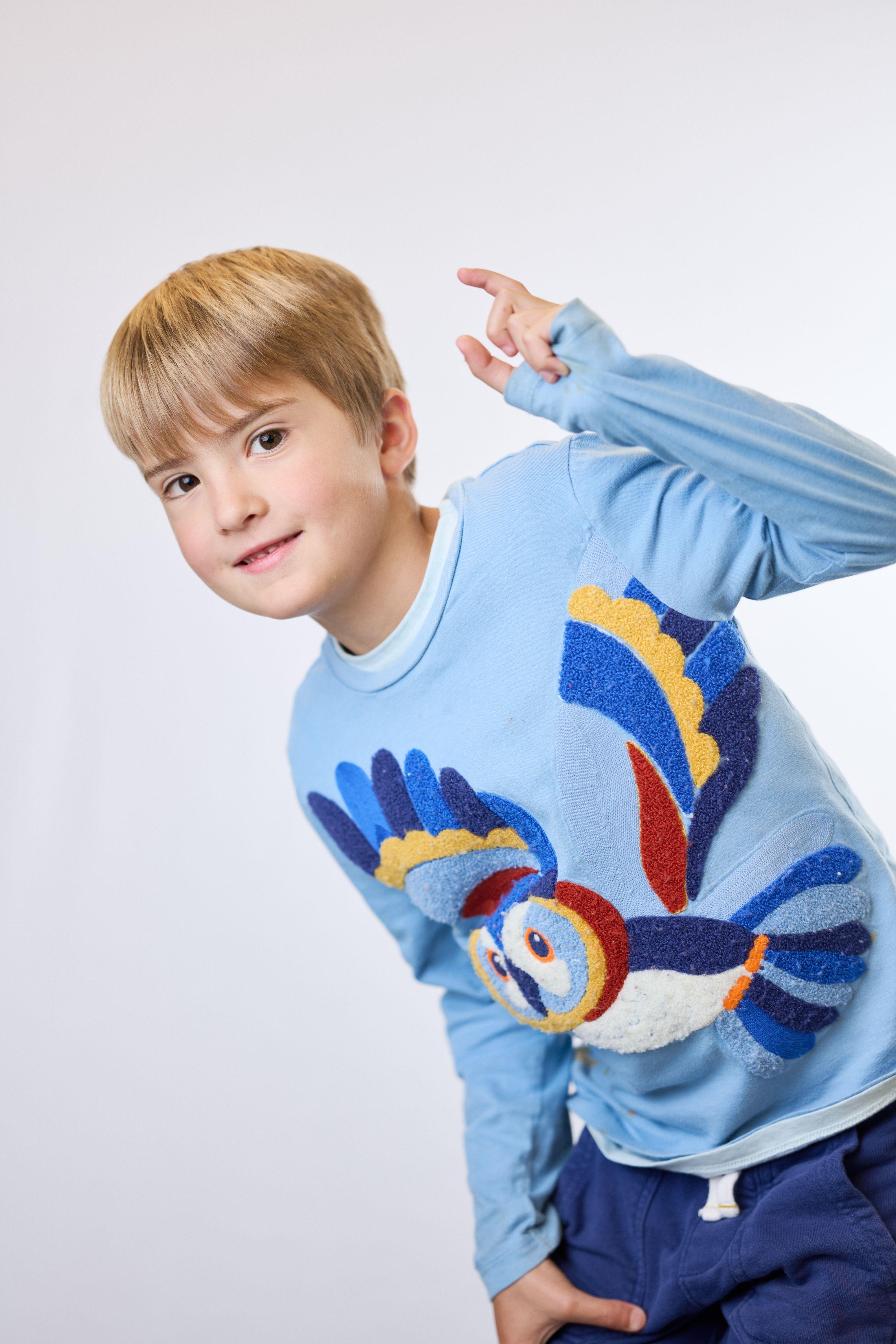 Boy in a blue sweater with a knitted parrot on it, pointing upward on a plain studio backdrop — Mobile photo studio, Austin A boy in a blue sweater with a knitted parrot on it, pointing upward on a plain studio backdrop