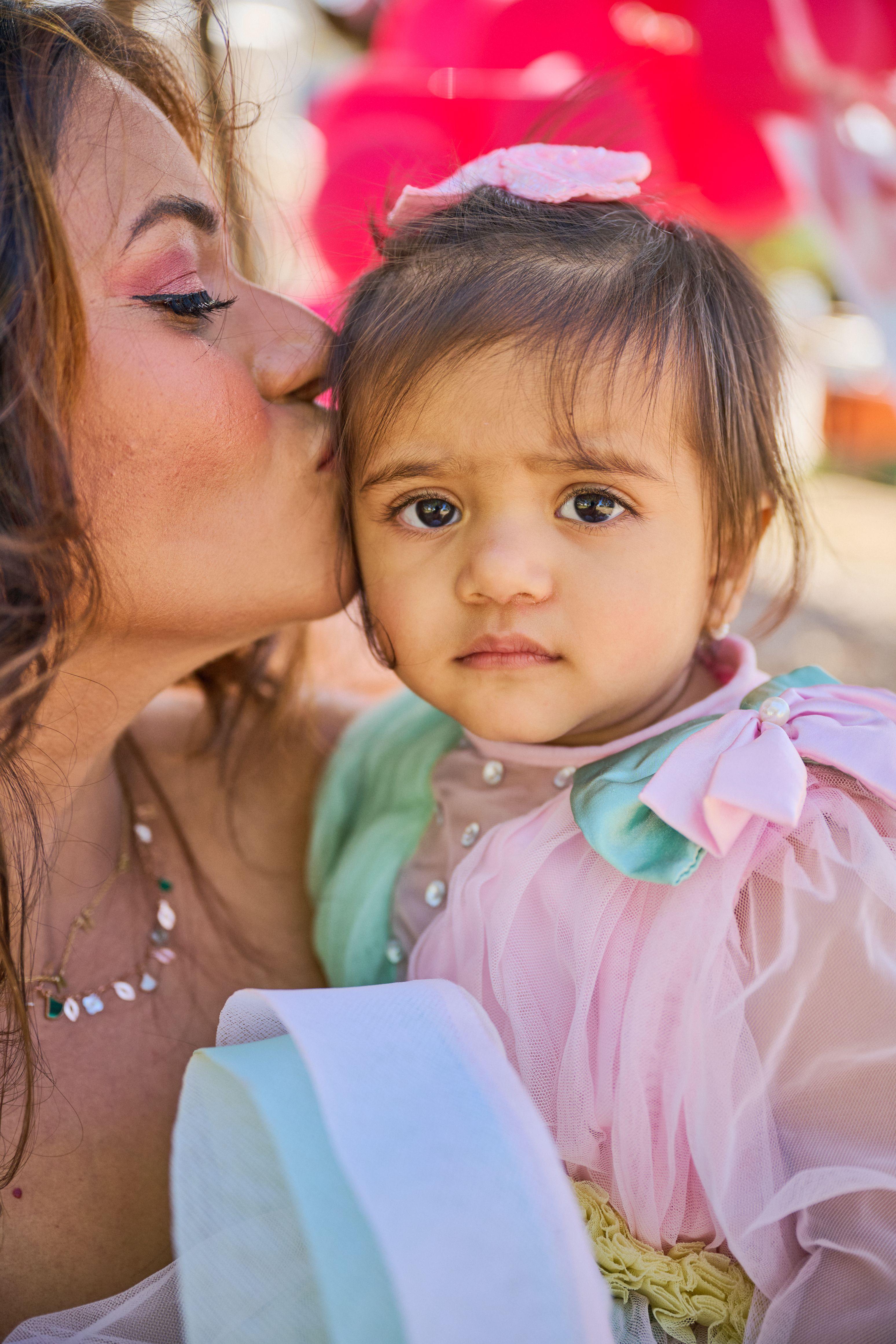 Mother kissing her toddler's cheek at a birthday party, the child looking to camera — Family Parties photography, Austin A mother kissing her toddler's cheek at a birthday party, the child looking to camera.