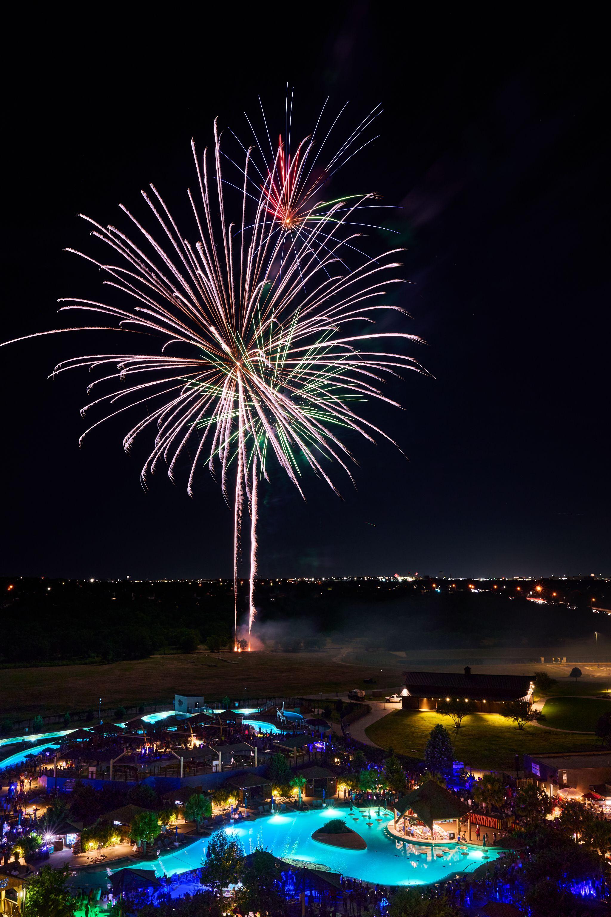Large white firework burst over a dark landscape with distant lights — Festival photography, Austin A large white firework burst over a dark landscape with distant lights.