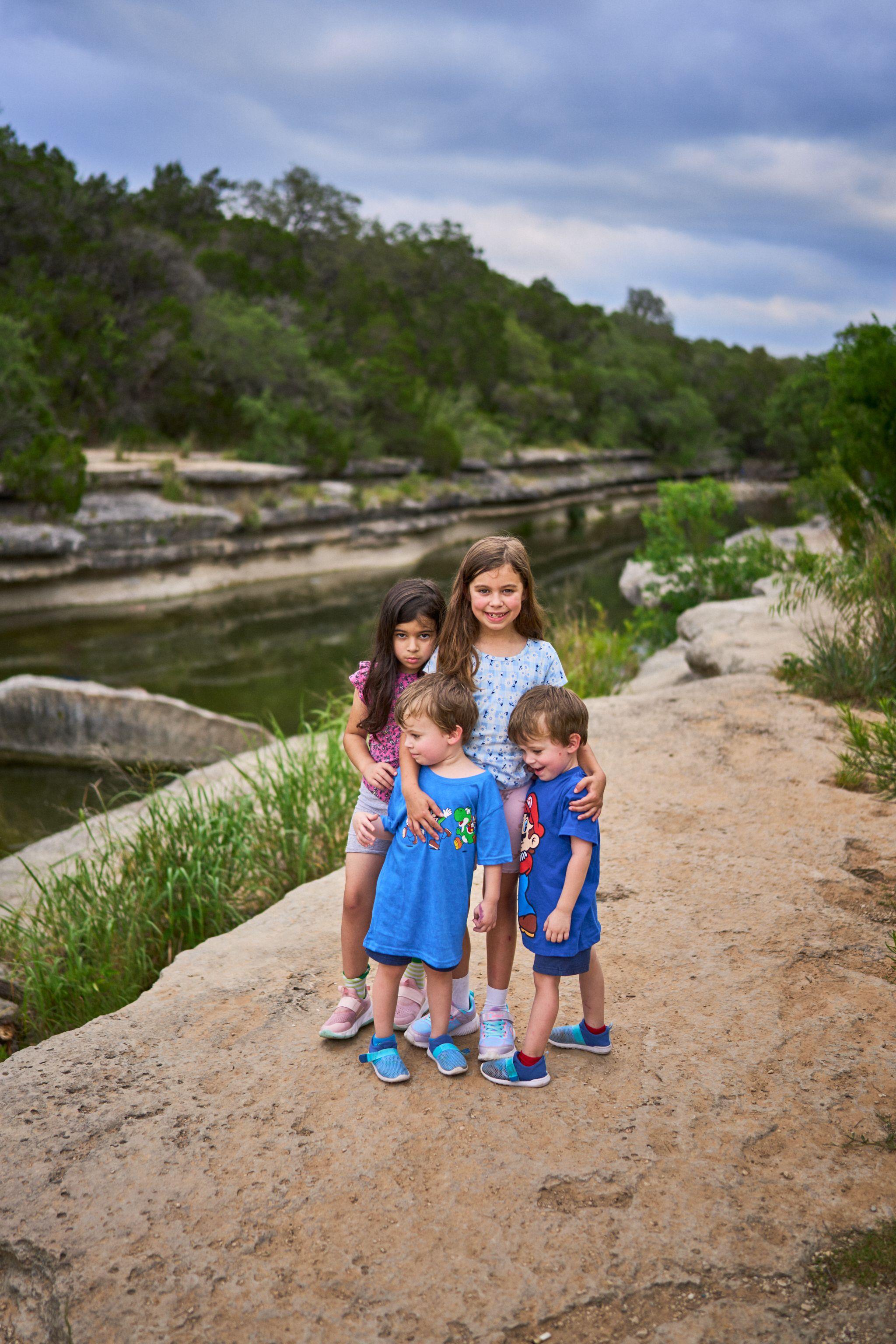Four children posed together on a limestone bank above a green creek — Bull Creek District Park photography, Austin Four children posed together on a limestone bank above a green creek.