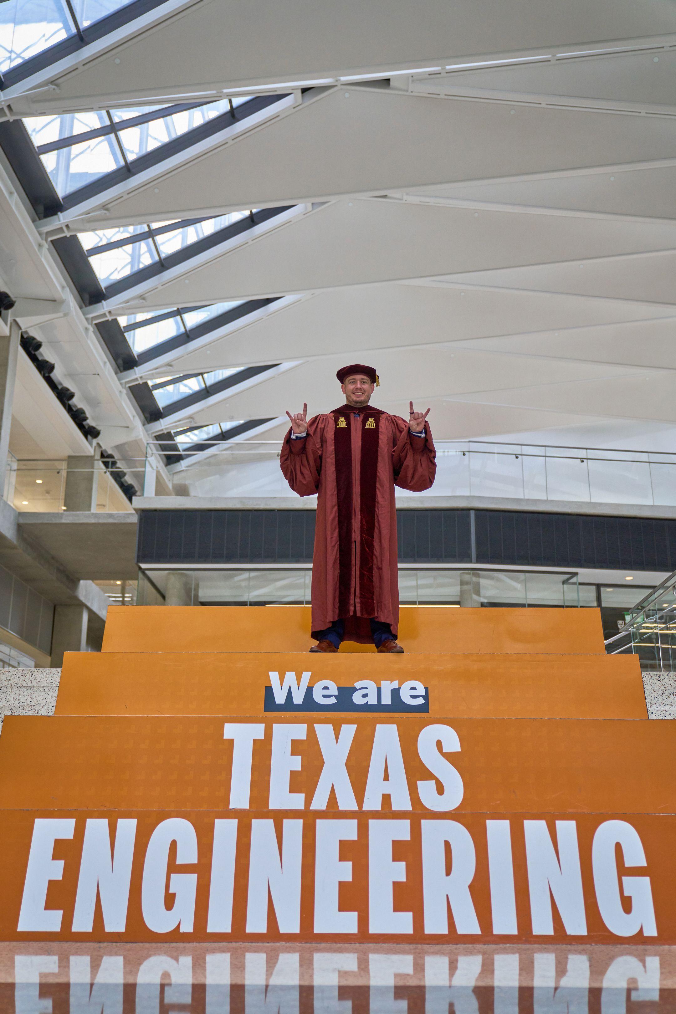 Graduate in a maroon gown throwing horns on the steps below a 'We are Texas Engineering' banner — Graduation & Prom photography, Austin A graduate in a maroon gown throwing horns on the steps below a 'We are Texas Engineering' banner.