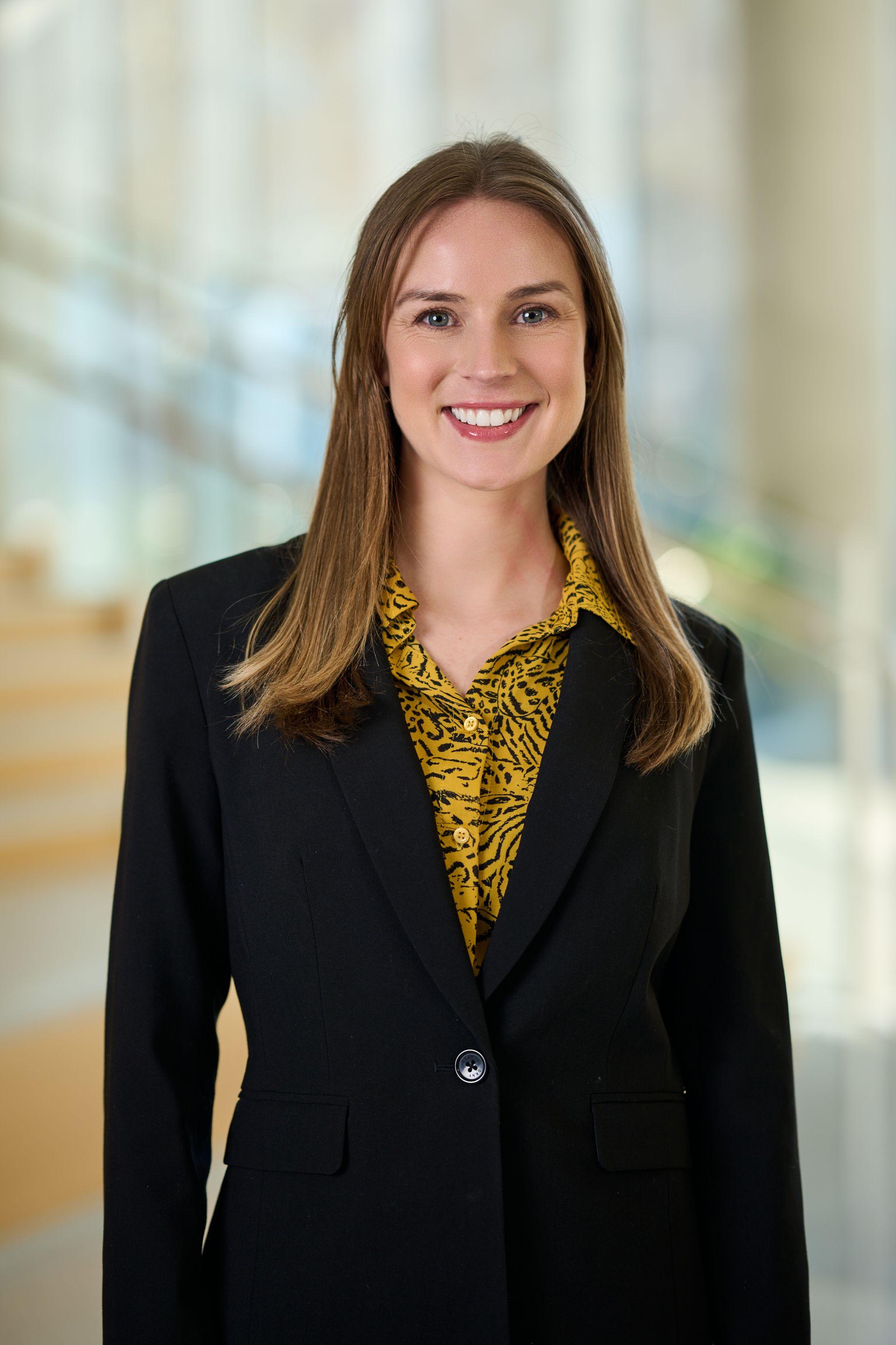 Woman in a black blazer over a patterned gold blouse, photographed — Mobile photo studio, Austin A woman in a black blazer over a patterned gold blouse, photographed against a blurred office interior