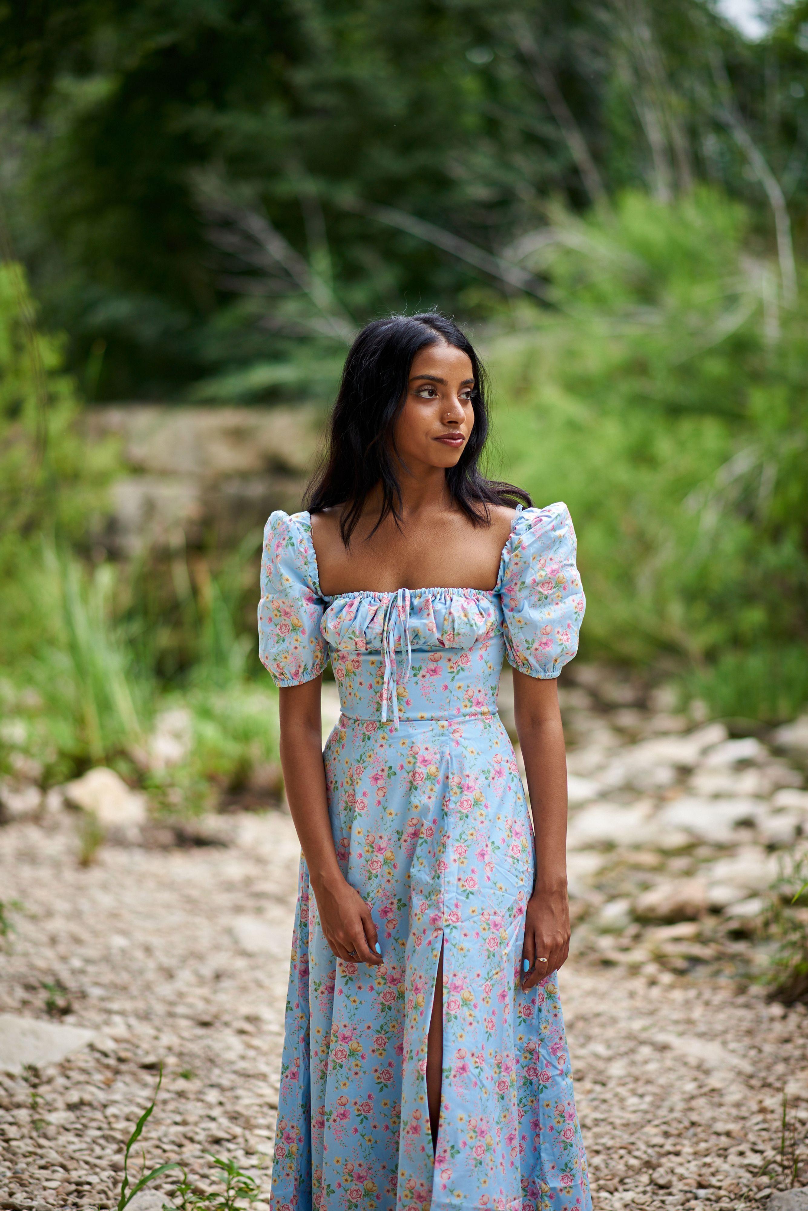 Woman in a pale blue floral prairie dress standing on a creek bed at Pease Park, green foliage — Fashion & editorial photography, Austin A woman in a pale blue floral prairie dress standing on a creek bed at Pease Park, green foliage behind her.