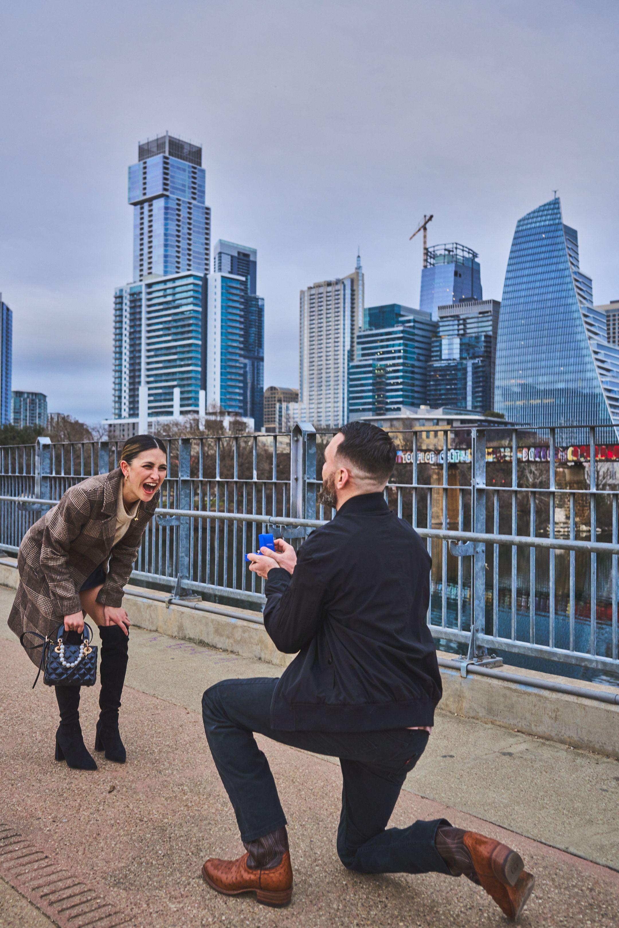 Man on one knee proposing on the Pfluger pedestrian bridge, the downtown Austin skyline — Engagement & Proposals photography, Austin A man on one knee proposing on the Pfluger pedestrian bridge, the downtown Austin skyline behind them.