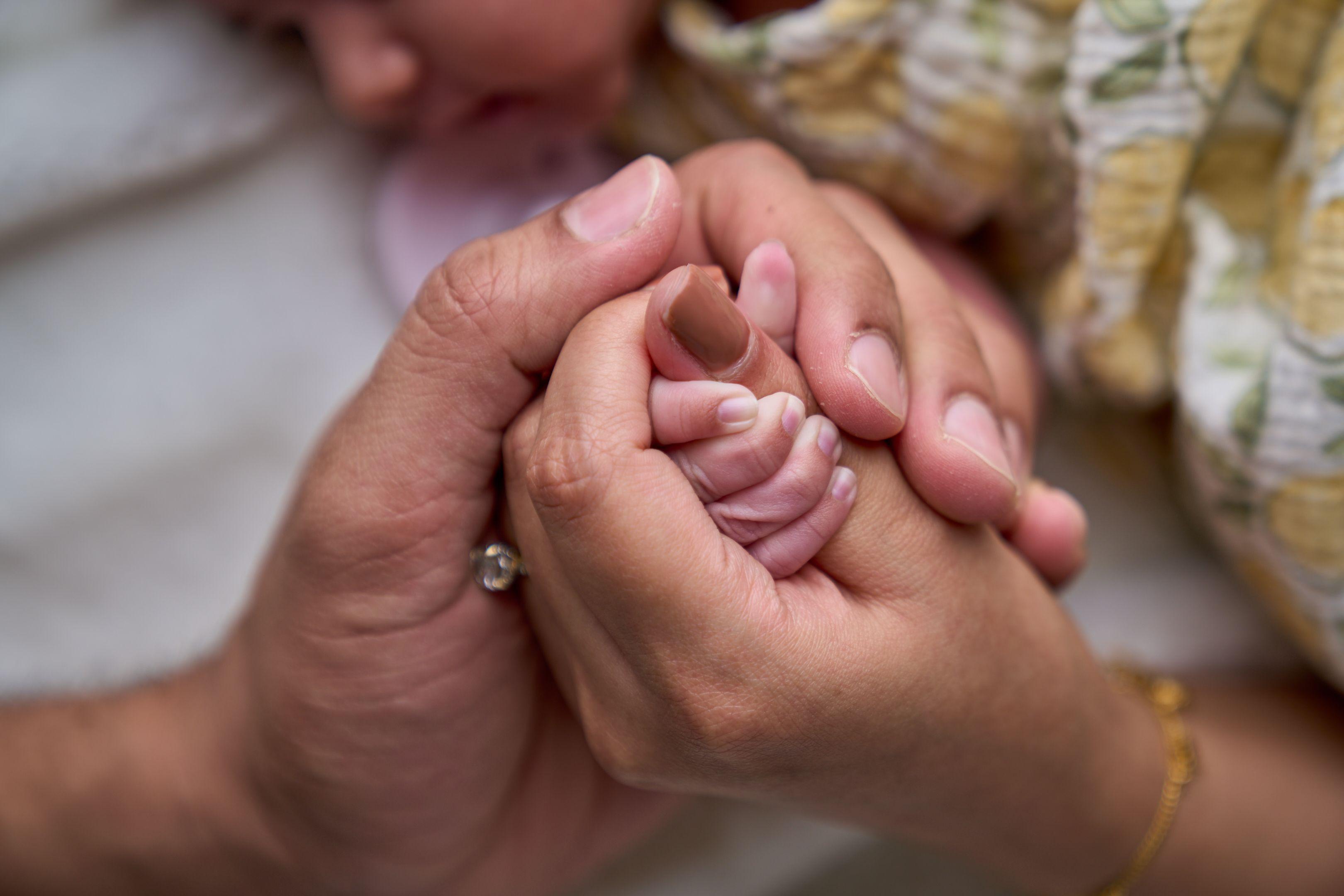 Newborn's fist held inside both of a parent's hands — Newborn photography, Austin A newborn's fist held inside both of a parent's hands.