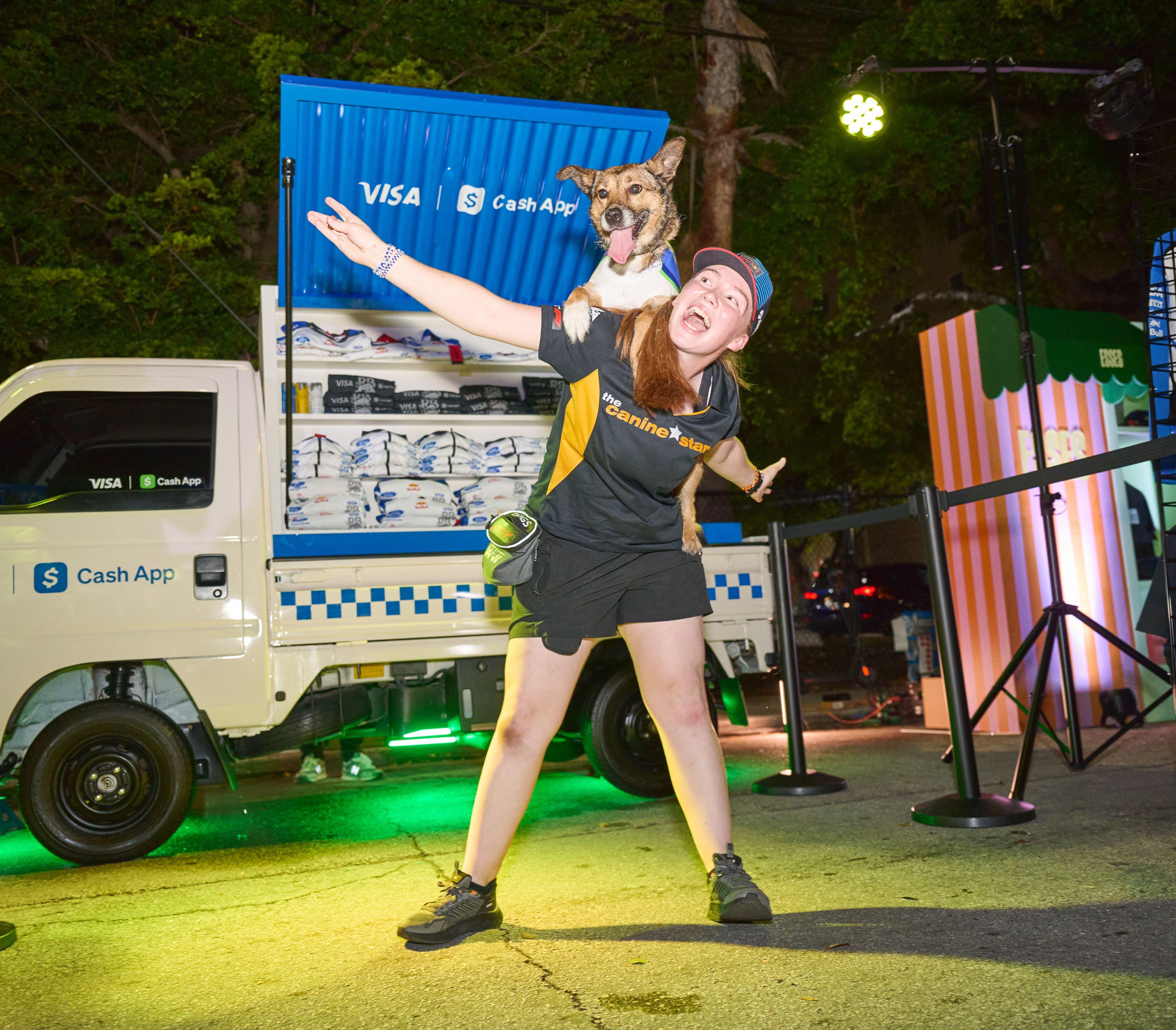 Brand staffer holding a dog on her shoulders in front of a Visa — Outdoor media photography, Austin A brand staffer holding a dog on her shoulders in front of a Visa and Cash App branded cooler truck lit green at night.