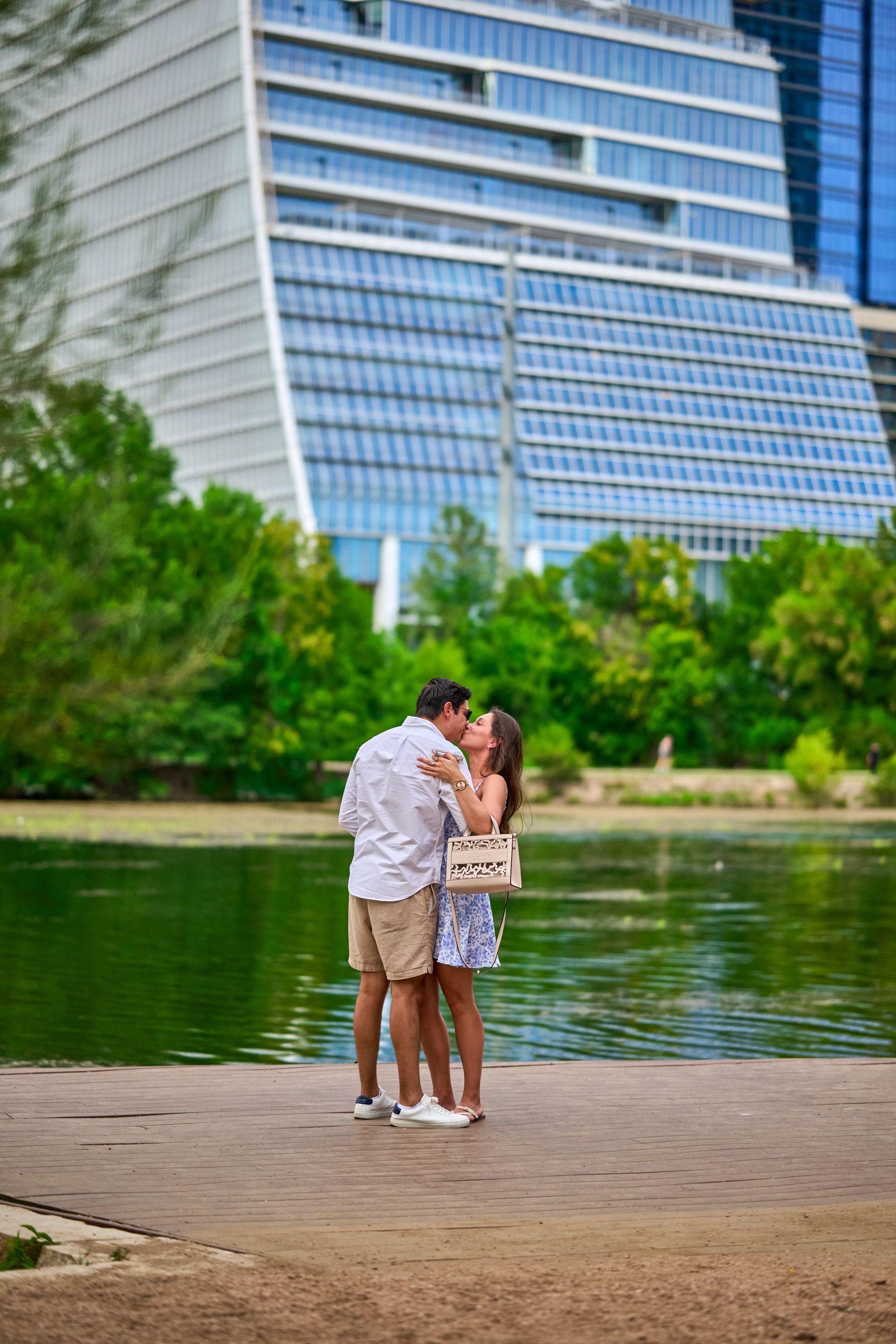 Couple embracing on the lakeside boardwalk beneath a curved glass tower — Butler Metro Park photography, Austin A couple embracing on the lakeside boardwalk beneath a curved glass tower.