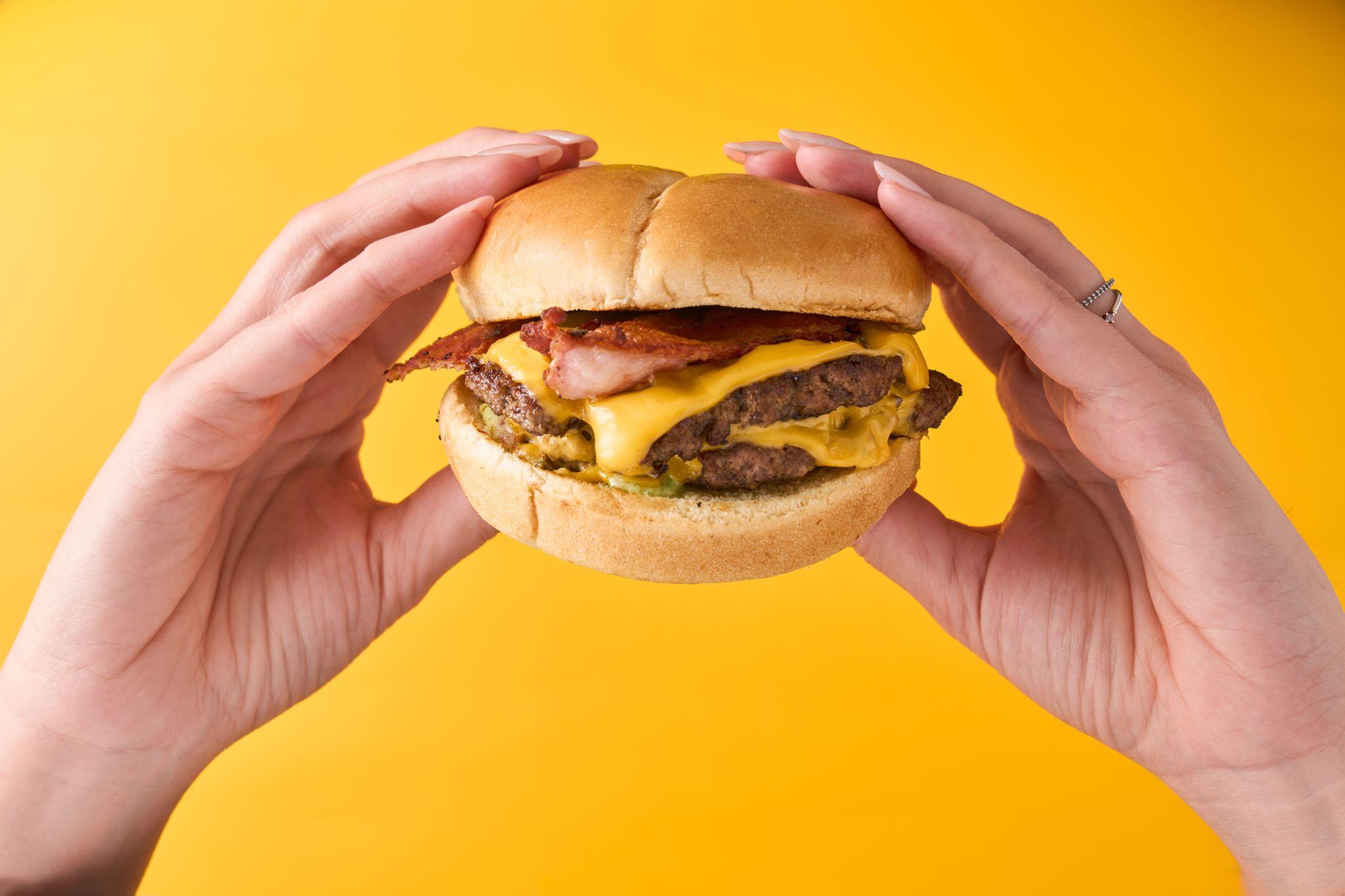 Double cheeseburger held in two hands against a bright yellow background — Food & restaurant photography, Austin A double cheeseburger held in two hands against a bright yellow background.