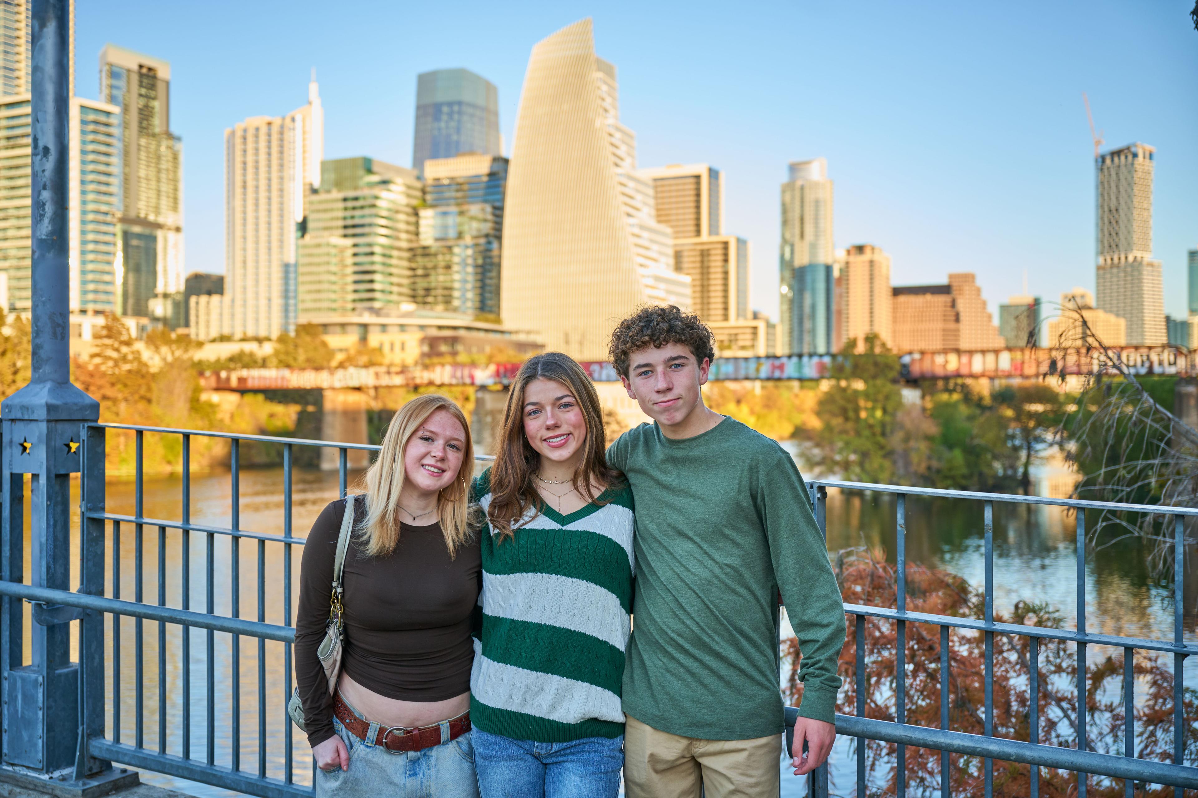 Three teenagers leaning on the Pfluger bridge railing at golden hour — Pfluger Pedestrian Bridge photography, Austin Three teenagers leaning on the Pfluger bridge railing at golden hour with the downtown Austin skyline behind them