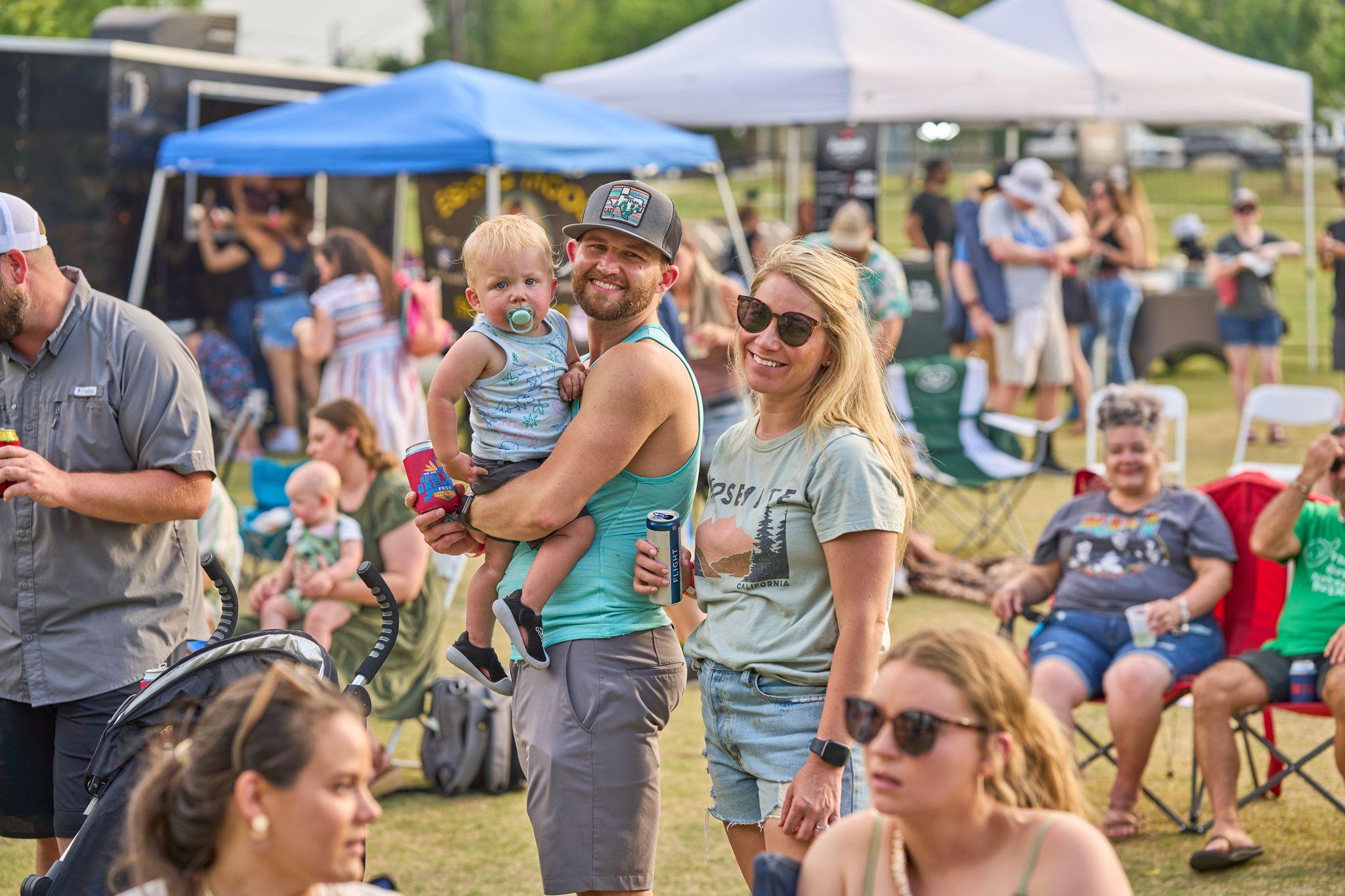 Father holding a toddler in a festival crowd beside friends with drinks — Festival photography, Austin A father holding a toddler in a festival crowd beside friends with drinks.
