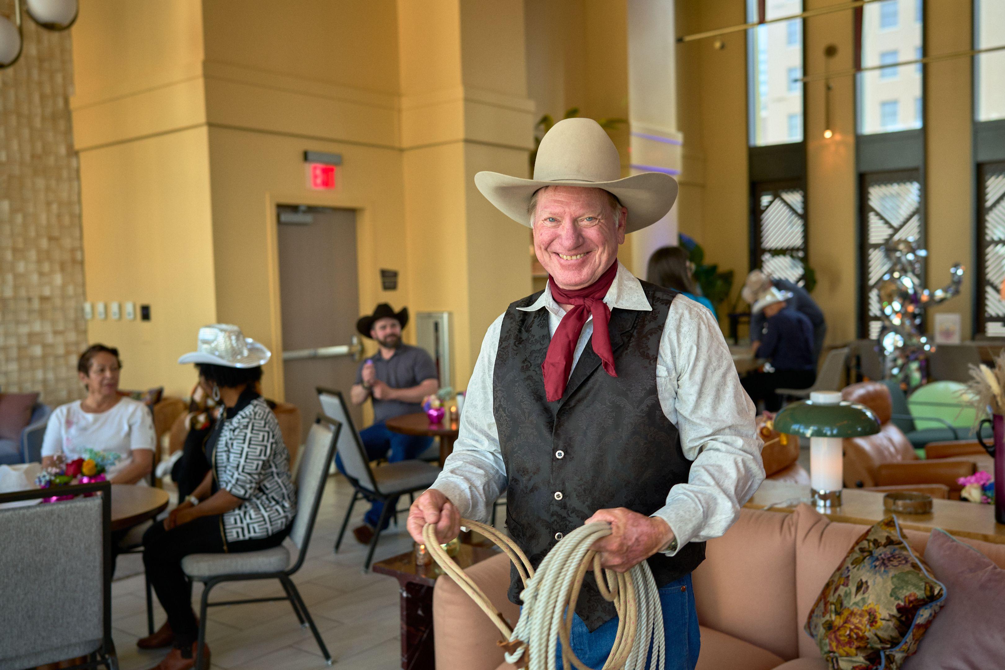 Rope-trick performer in a cowboy hat and red neckerchief holding a coiled lasso indoors — Business Parties photography, Austin A rope-trick performer in a cowboy hat and red neckerchief holding a coiled lasso indoors.