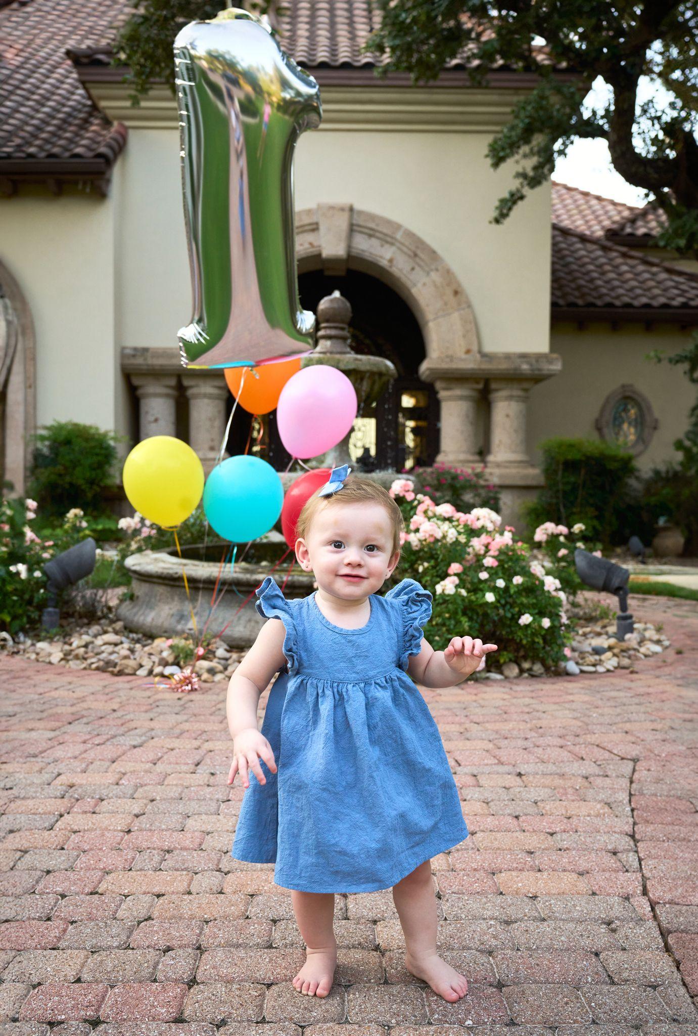 Toddler in a blue dress running past balloons in a courtyard with a fountain — Family Parties photography, Austin A toddler in a blue dress running past balloons in a courtyard with a fountain.