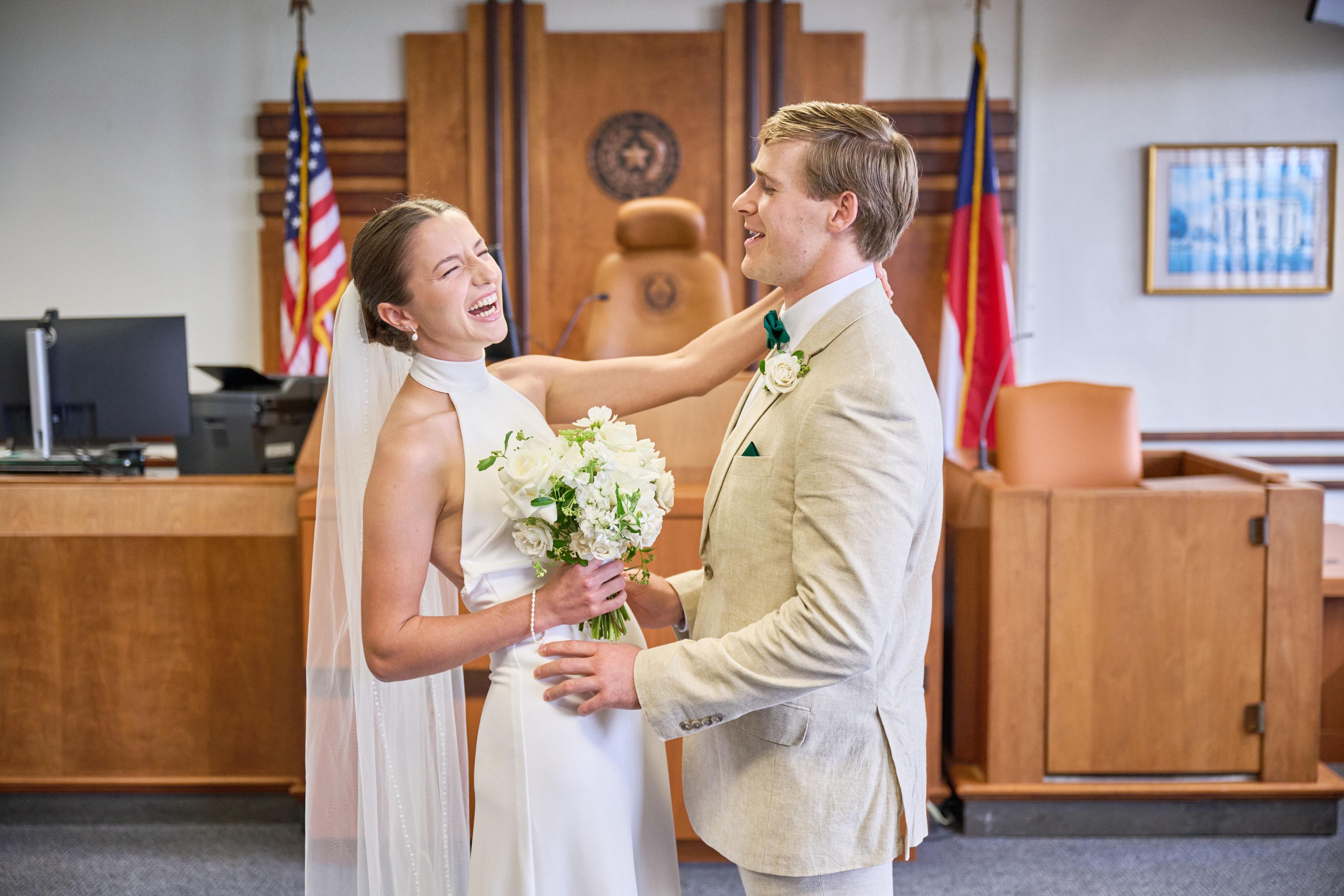 Bride reaching up to her groom's face in the courthouse ceremony room, flags behind them — Weddings photography, Austin A bride reaching up to her groom's face in the courthouse ceremony room, flags behind them.