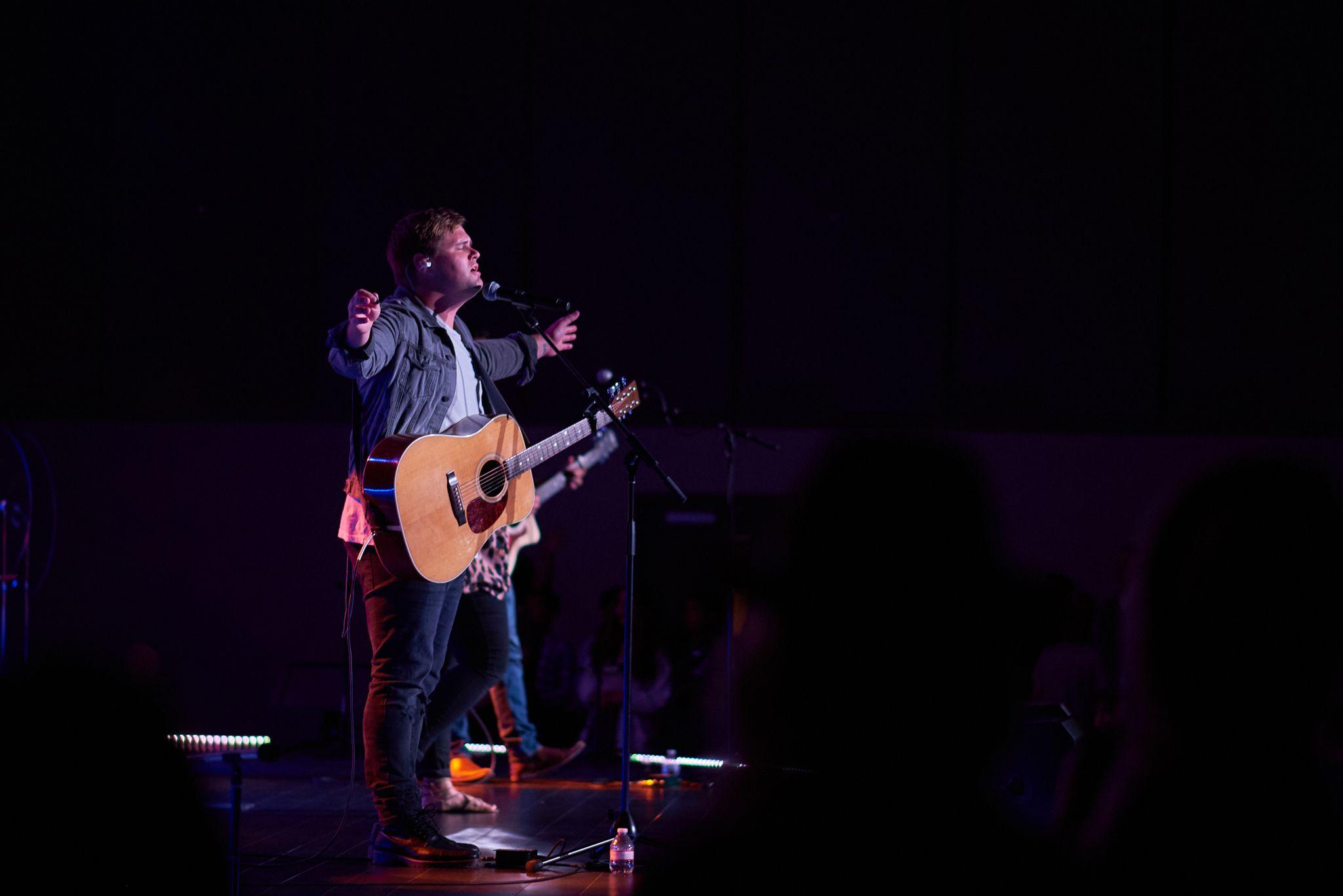 Singer with an acoustic guitar performing alone on a purple-lit stage — Live music photography, Austin A singer with an acoustic guitar performing alone on a purple-lit stage.