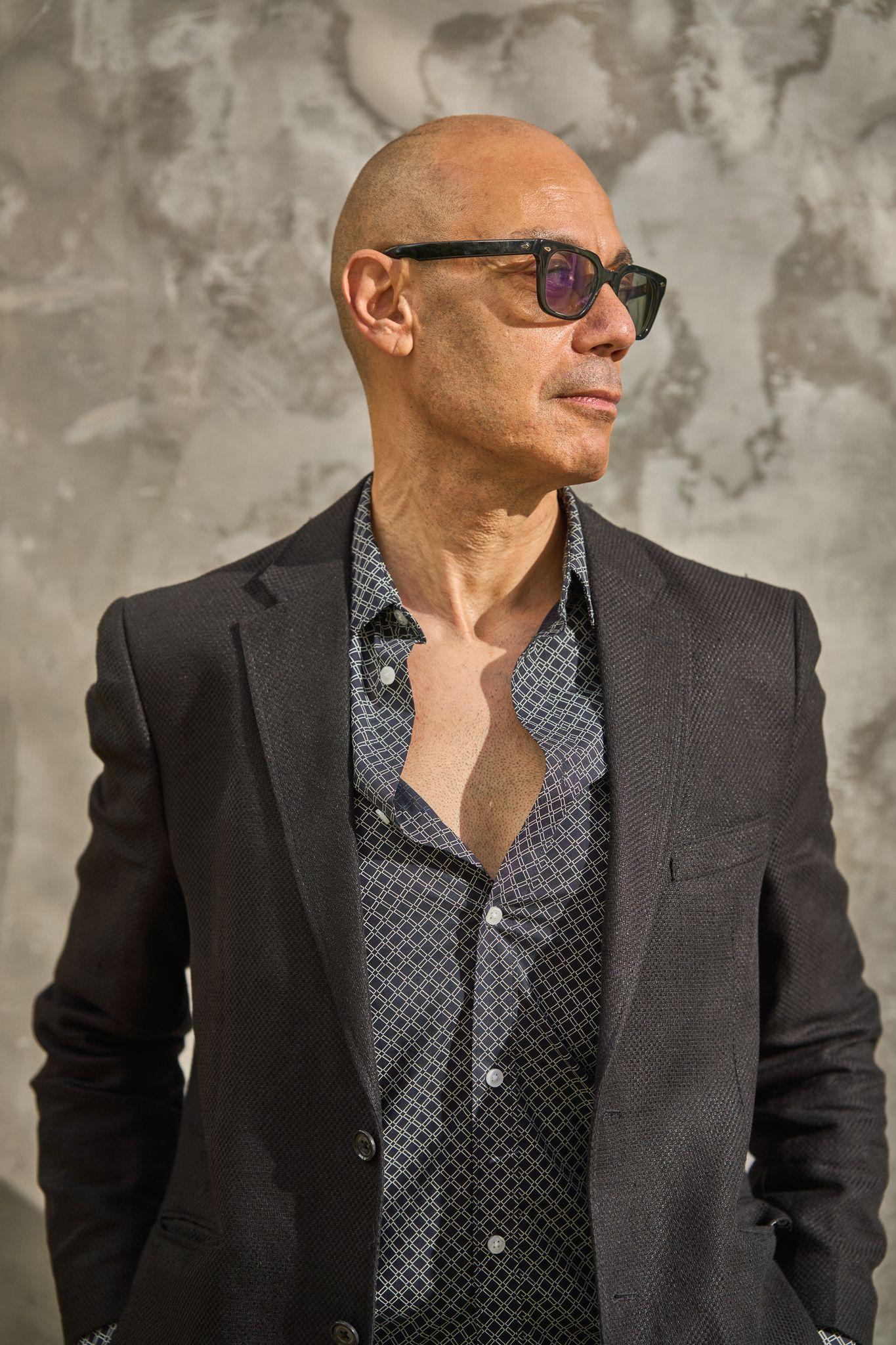 Man in a gray suit and patterned shirt with sunglasses against a stone wall — Headshot photography, Austin A man in a gray suit and patterned shirt with sunglasses against a stone wall.