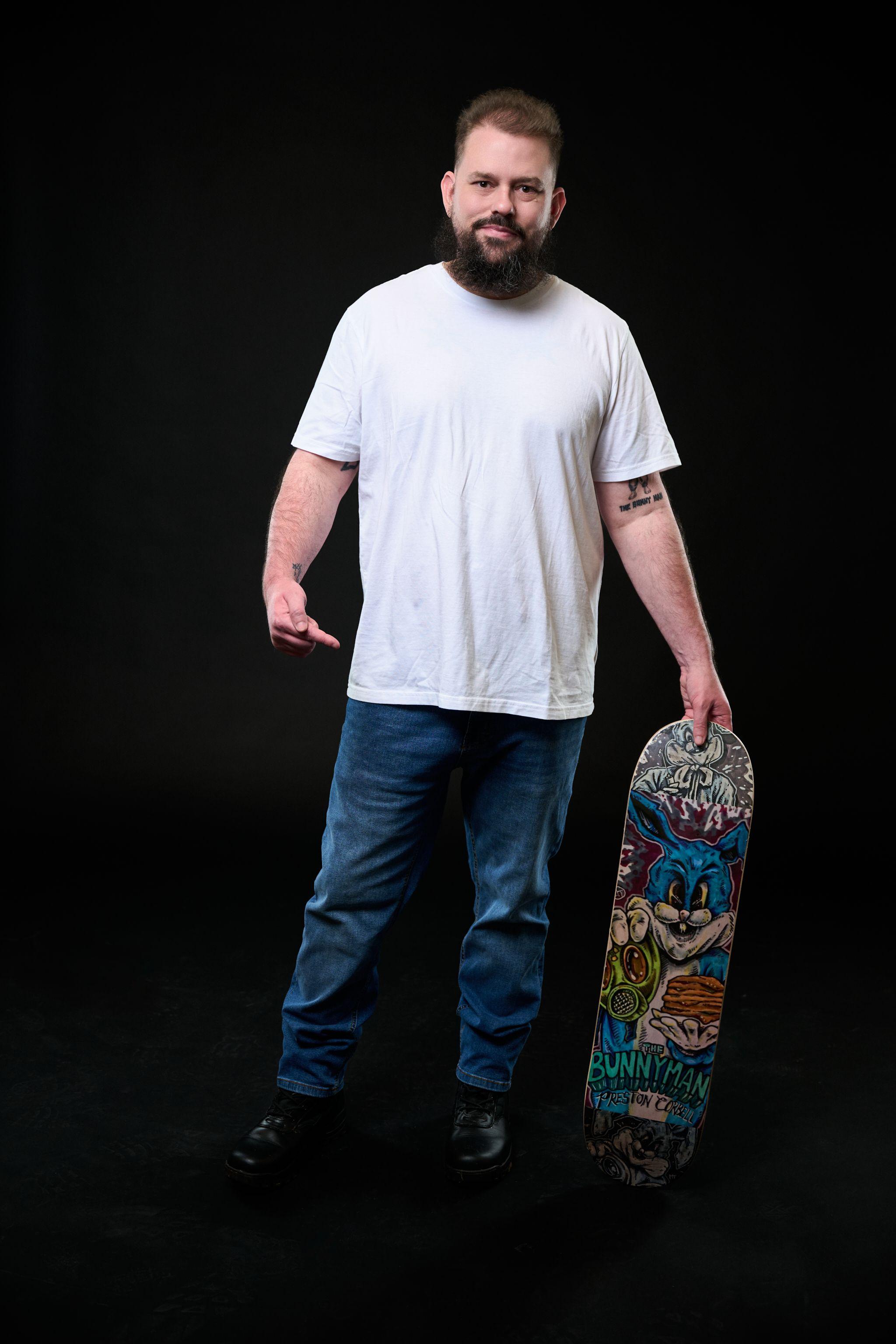 Bearded man in a white tee and jeans holding a skateboard against black seamless — Commercial photo studio, Austin Bearded man in a white tee and jeans holding a skateboard against black seamless