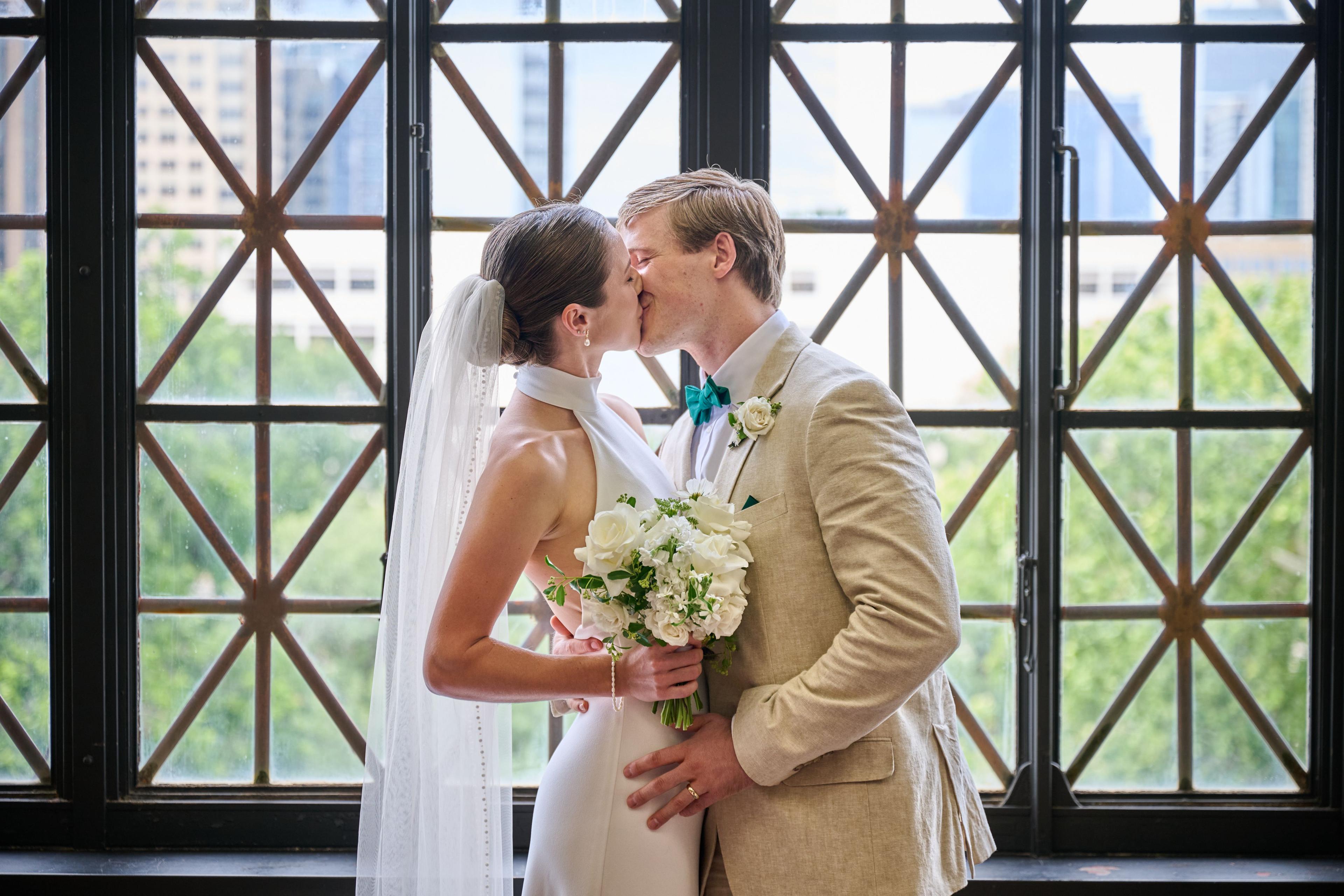 Couple kissing in front of a tall latticed window, the bride holding a white bouquet — Weddings photography, Austin A couple kissing in front of a tall latticed window, the bride holding a white bouquet.