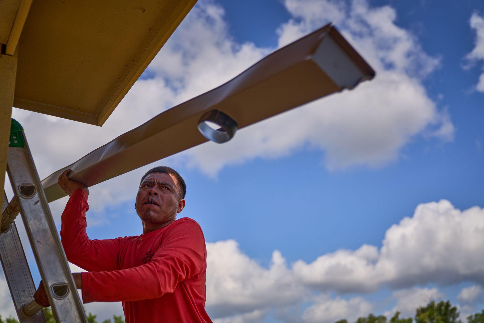Low-angle shot of a worker in a red long-sleeve shirt looking up beneath a steel beam — Industrial photography, Austin Low-angle shot of a worker in a red long-sleeve shirt looking up beneath a steel beam