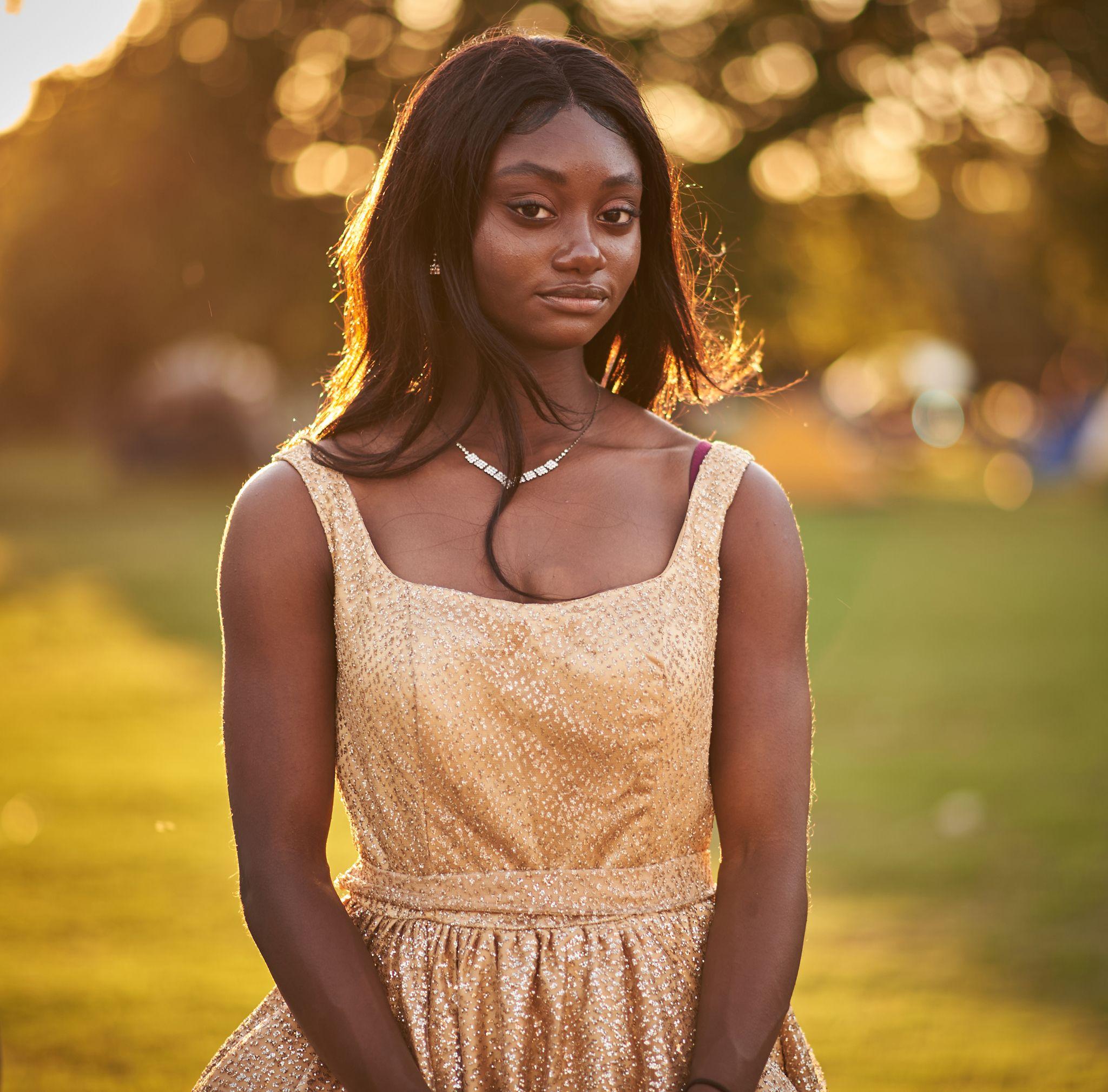 A woman in a gold sequinned dress photographed in a park at golden hour