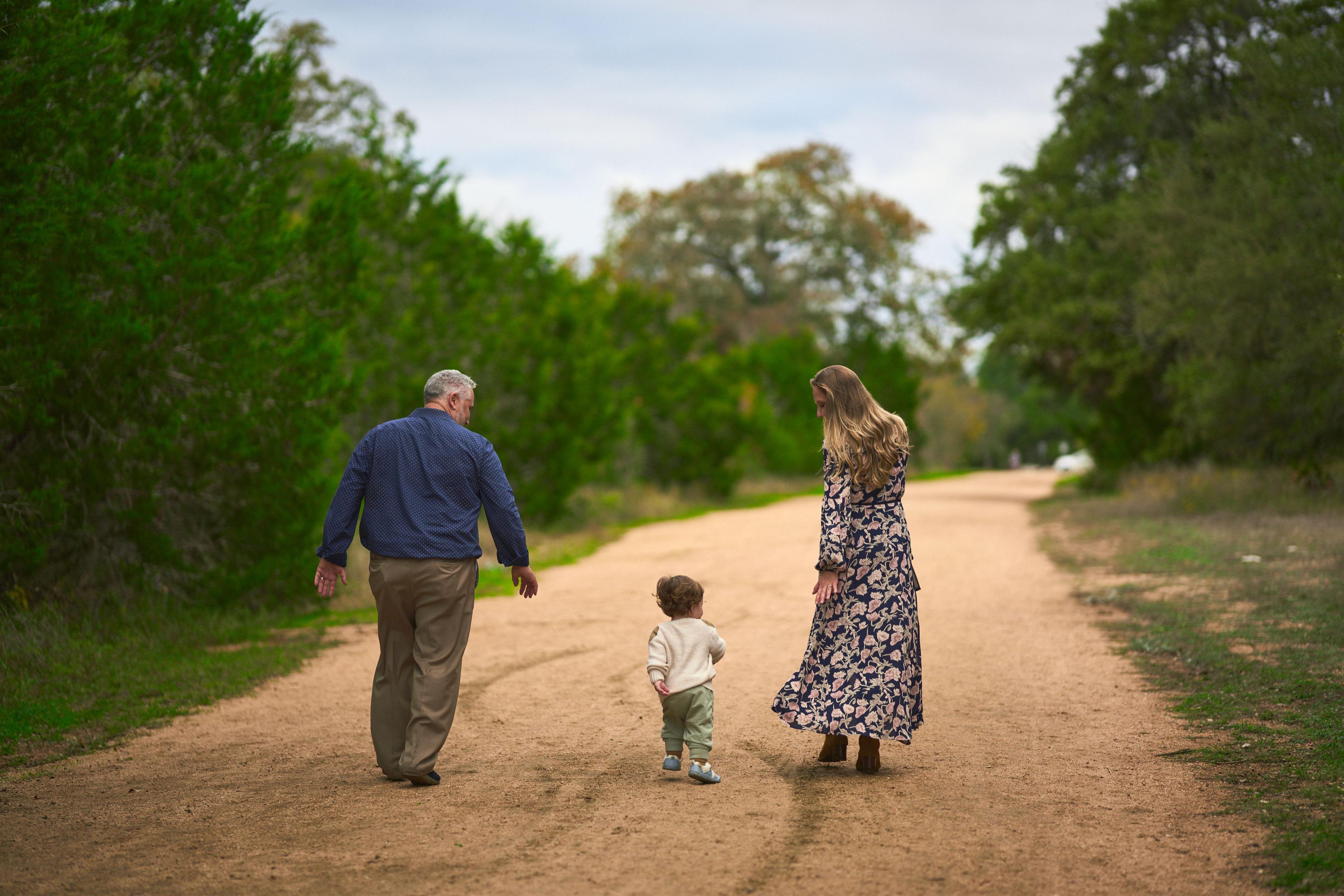 Grandfather, a toddler and a mother walking away down a pale caliche trail — Circle C Ranch photography, Austin A grandfather, a toddler and a mother walking away down a pale caliche trail on the Circle C greenbelt