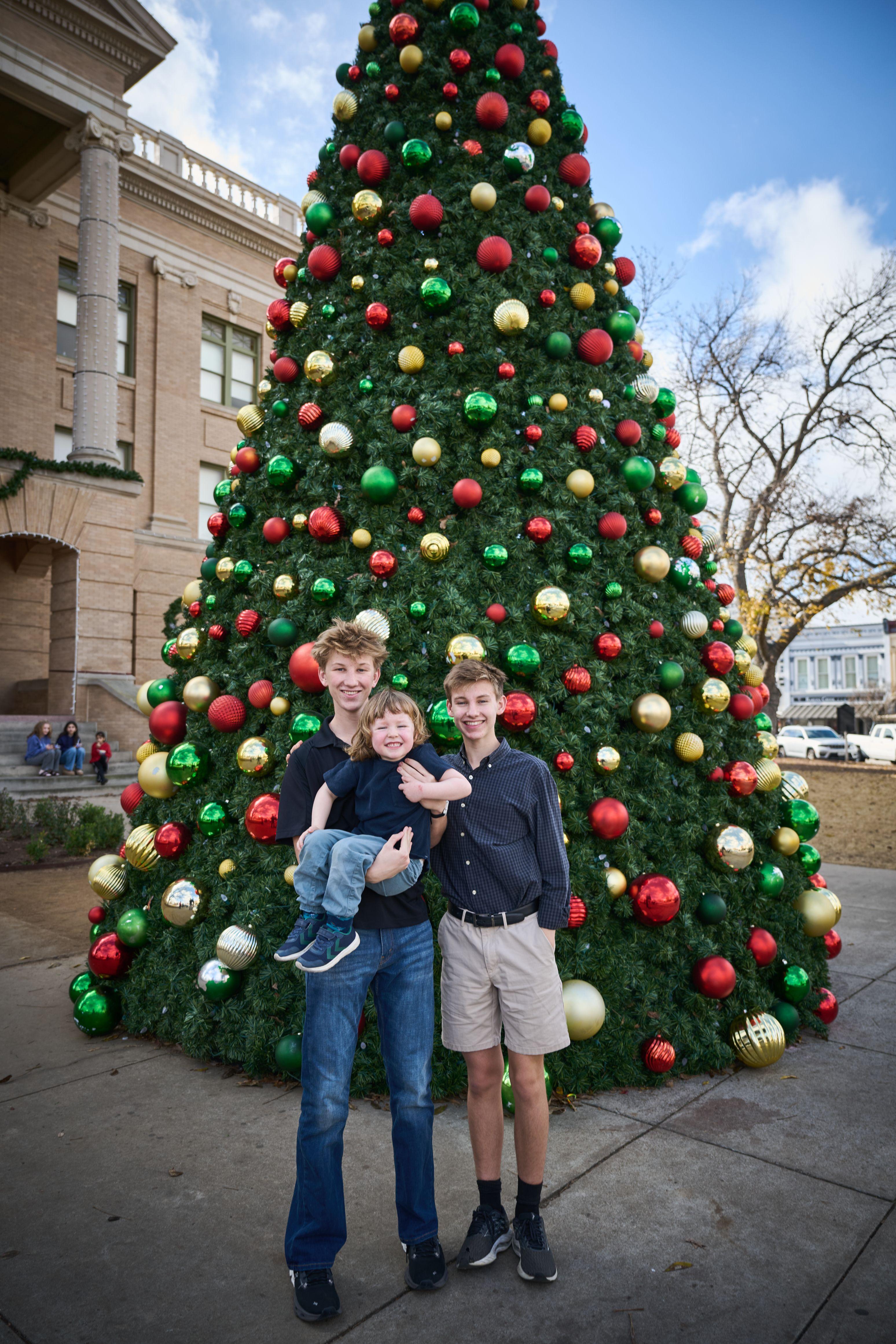 Father and two sons in front of a towering red and green Christmas tree — Georgetown Downtown photography, Austin A father and two sons in front of a towering red and green Christmas tree.