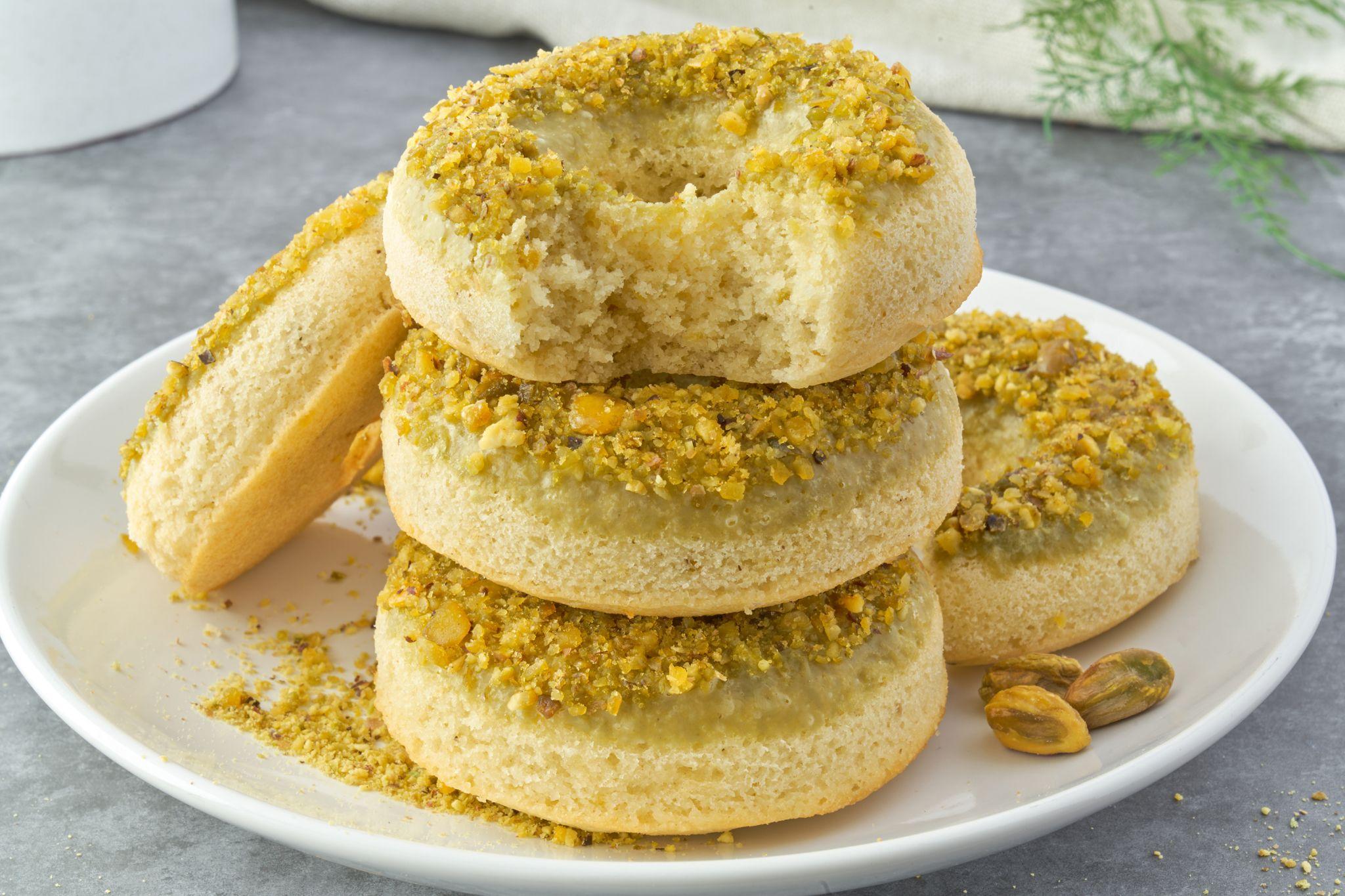 Stack of three pistachio-crusted glazed doughnuts on a white plate — E-commerce & apparel photography, Austin Stack of three pistachio-crusted glazed doughnuts on a white plate