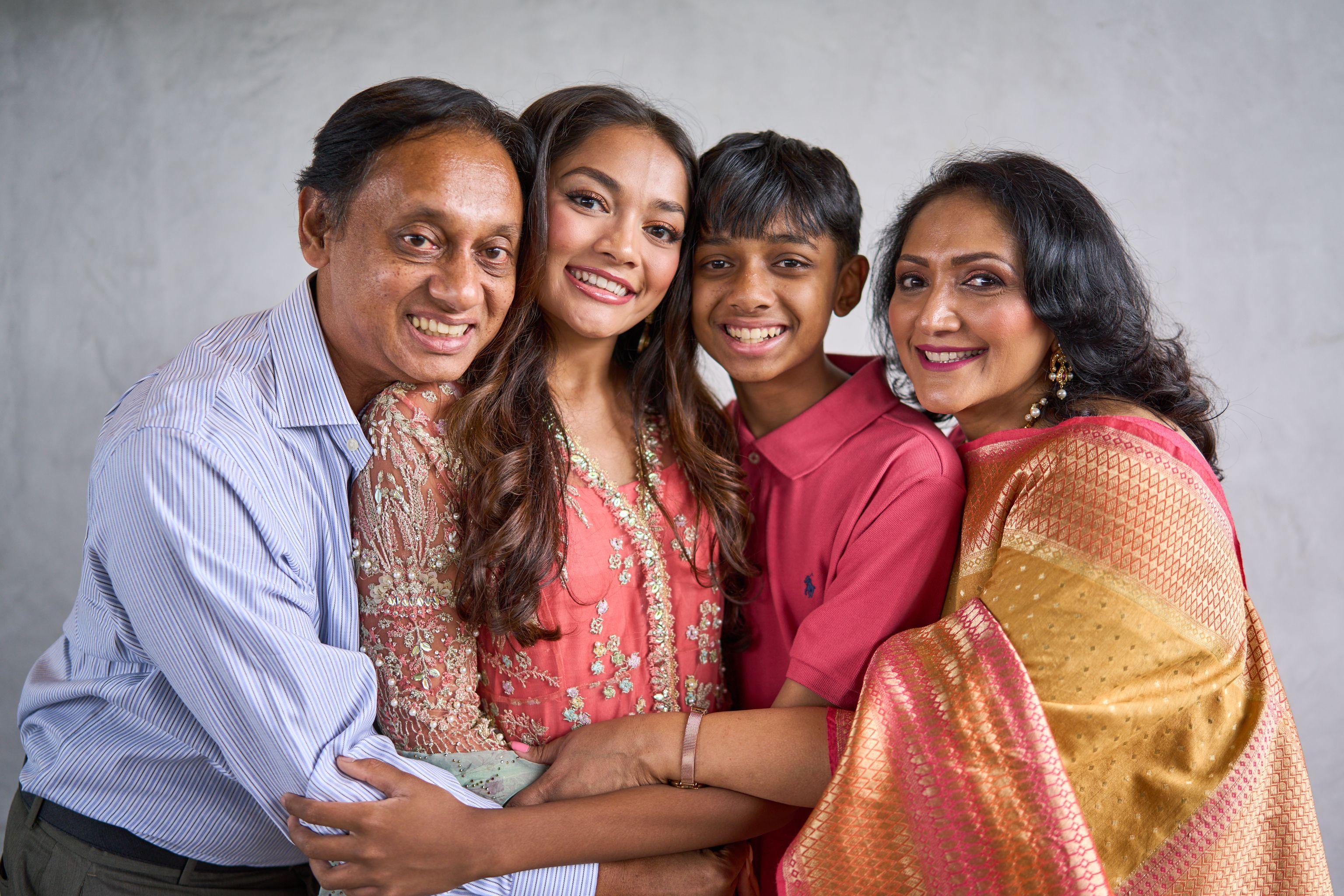 Family of four in coral and gold South Asian dress posed close together — Family Portraits photography, Austin A family of four in coral and gold South Asian dress posed close together.