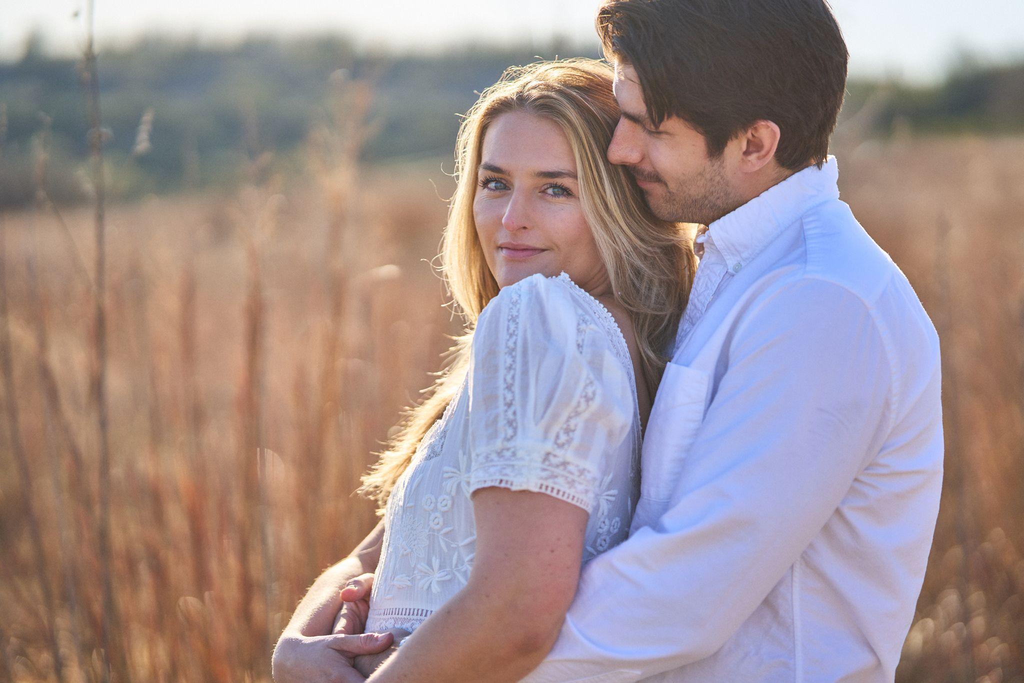 Couple embracing in tall dry grass at sunset, she in white lace — Commons Ford Ranch photography, Austin A couple embracing in tall dry grass at sunset, she in white lace.