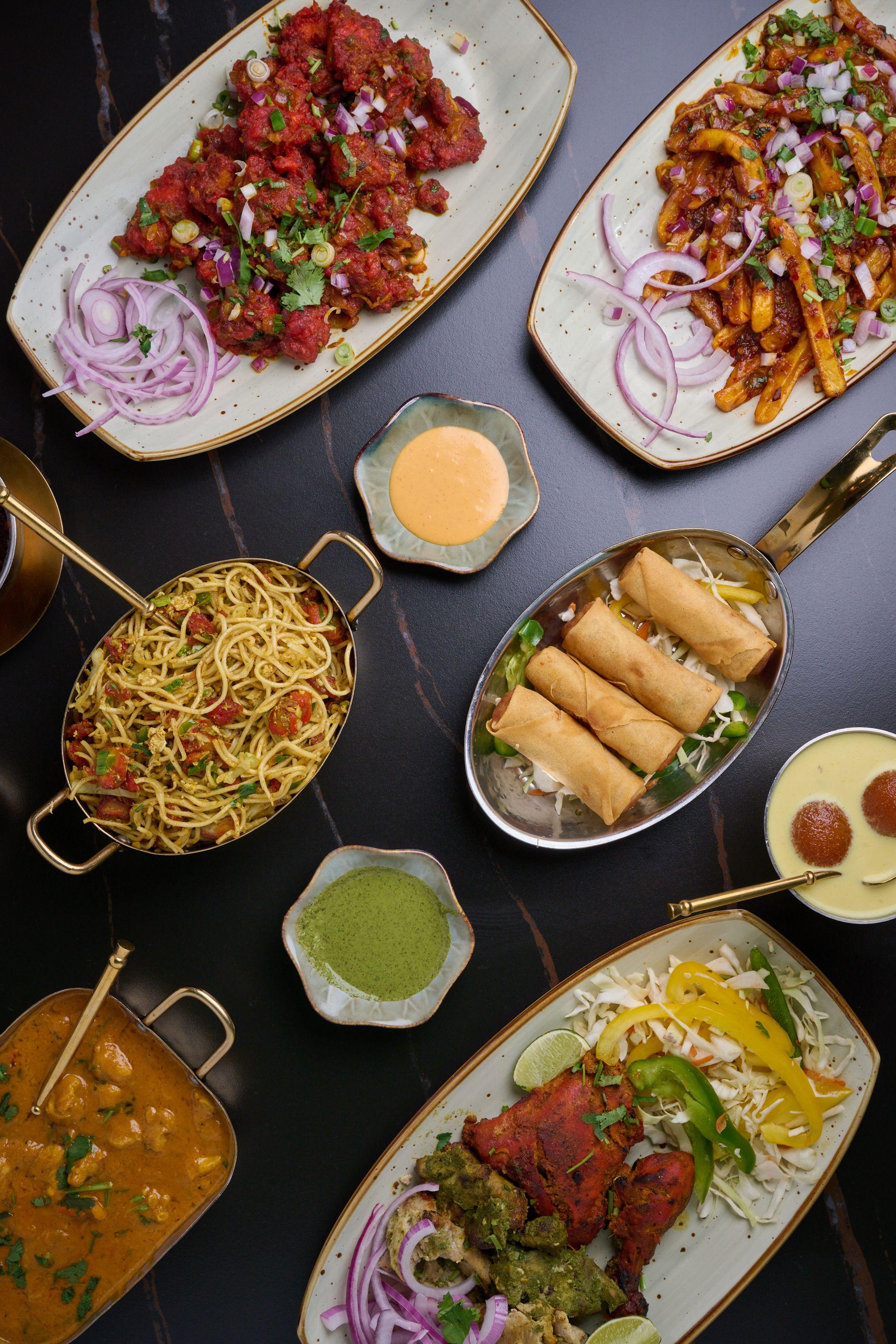 Overhead spread of Indian dishes — curries, noodles, samosas and chutneys on a dark table — Food & restaurant photography, Austin An overhead spread of Indian dishes — curries, noodles, samosas and chutneys on a dark table.