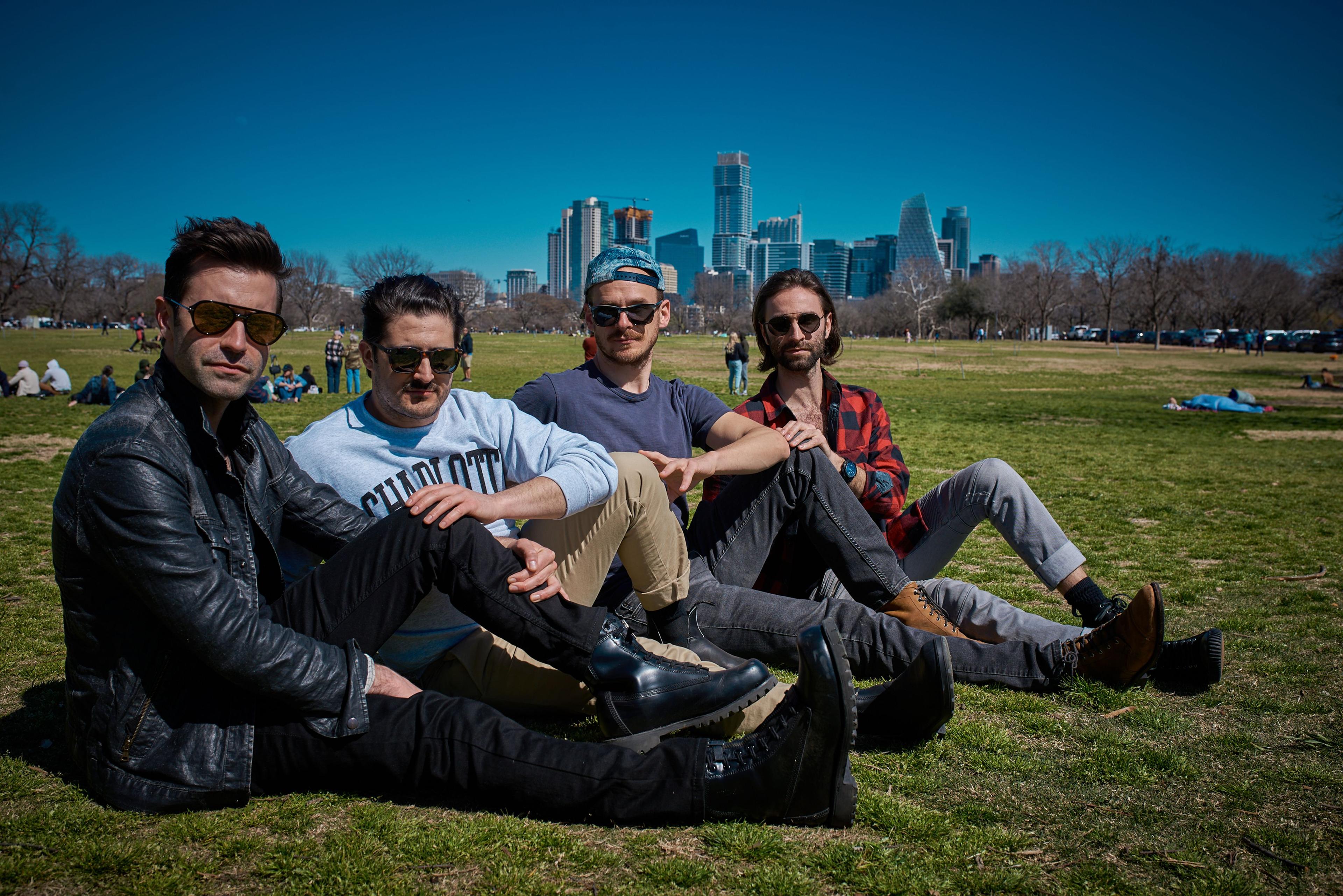 Four colleagues sitting on the grass in a park with the downtown Austin skyline behind them — Team offsite photography, Austin Four colleagues sitting on the grass in a park with the downtown Austin skyline behind them