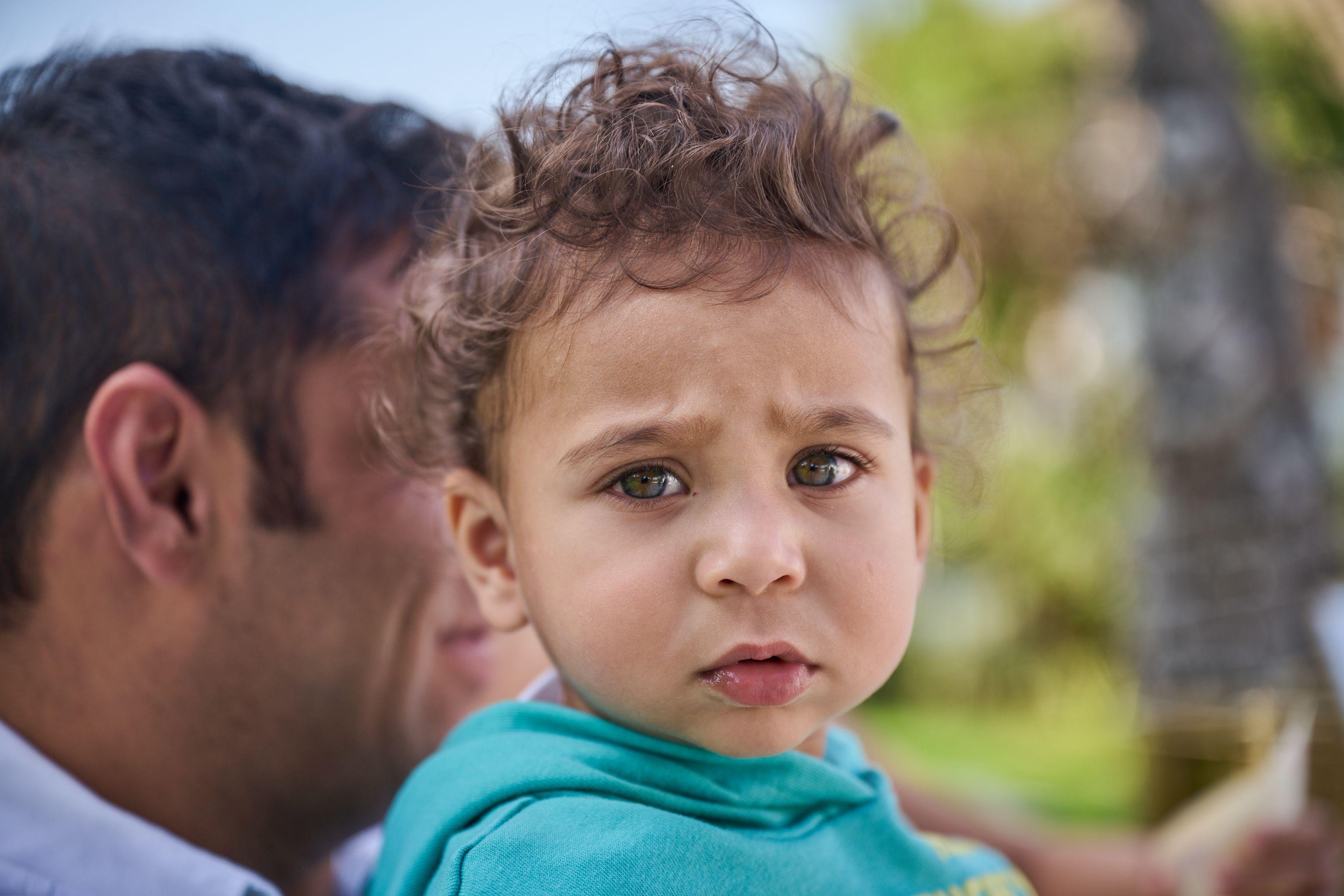 Close portrait of a curly-haired toddler in teal, frowning at camera — Kids Portraits photography, Austin A close portrait of a curly-haired toddler in teal, frowning at camera.