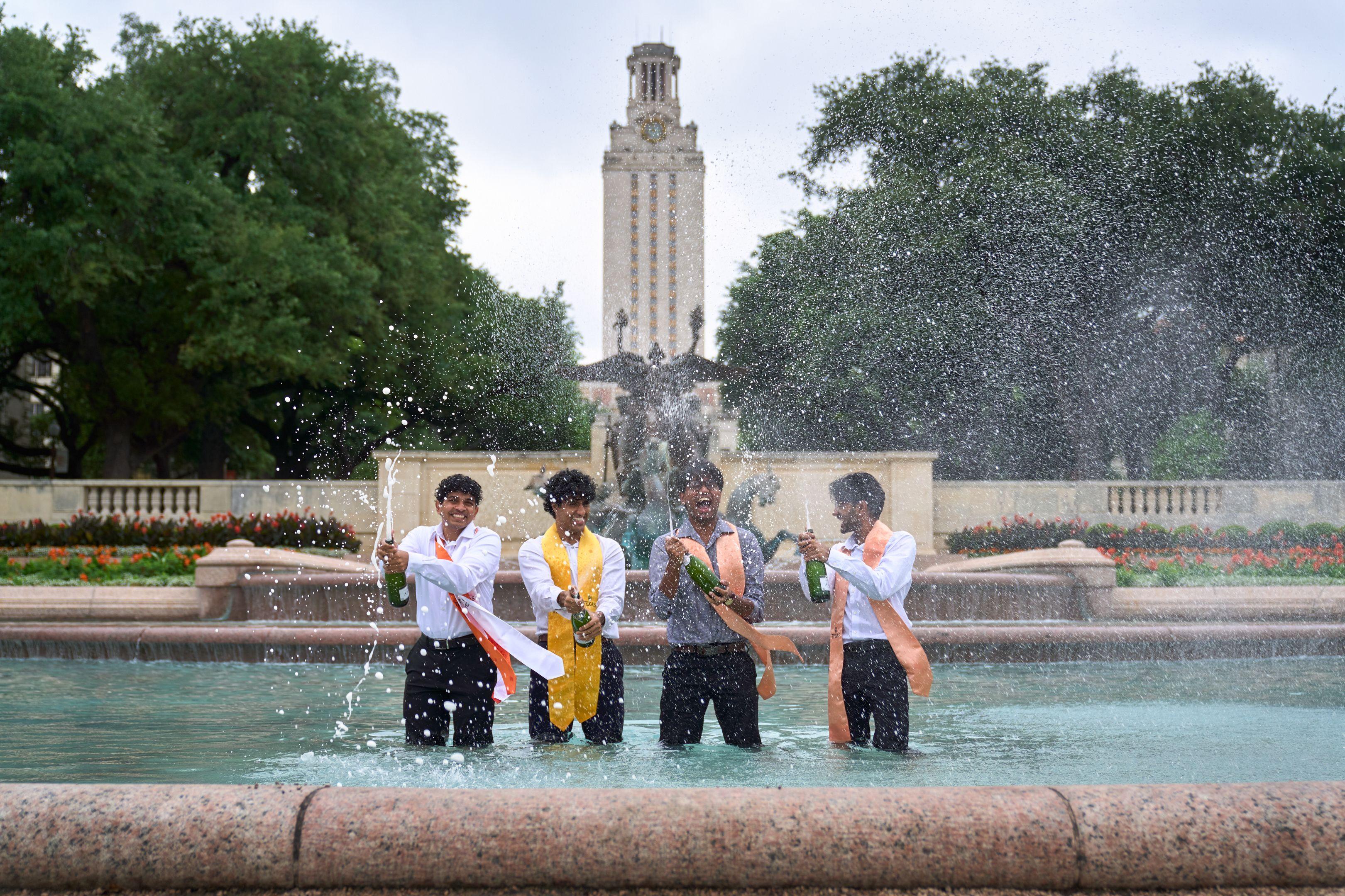 Graduates in stoles standing in the UT Austin fountain spraying champagne, the Tower — Graduation & Prom photography, Austin Graduates in stoles standing in the UT Austin fountain spraying champagne, the Tower behind them.