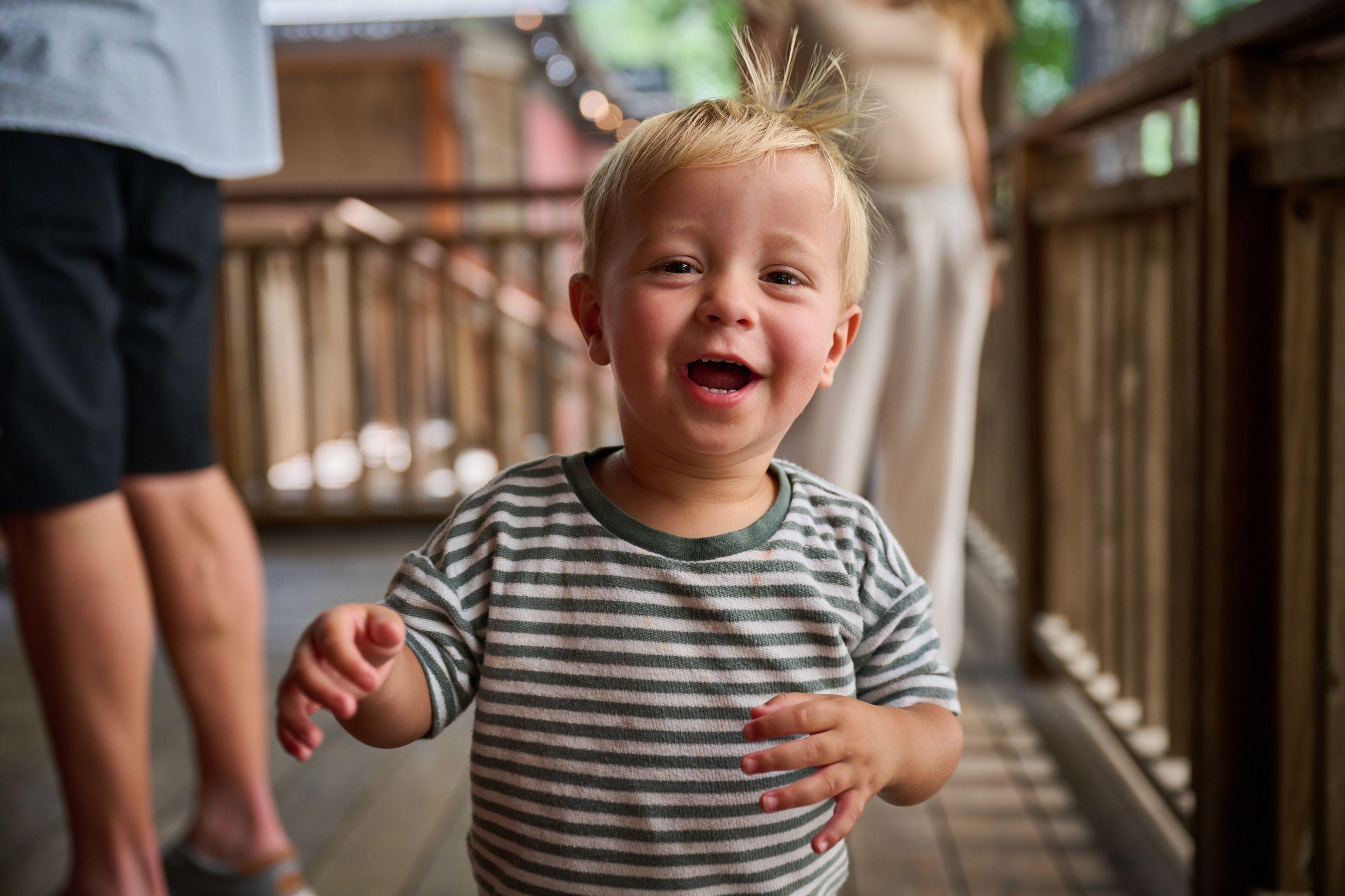 Laughing toddler in a striped shirt on a porch, hair sticking up — Kids Portraits photography, Austin A laughing toddler in a striped shirt on a porch, hair sticking up.