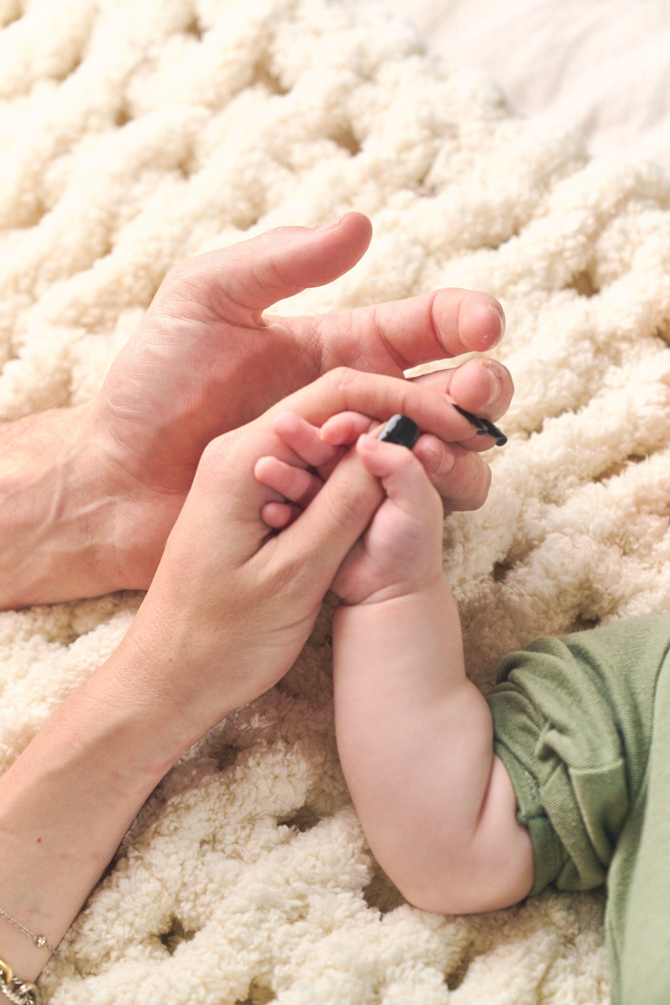 Newborn's hand curled around an adult finger on a chunky cream blanket — Newborn photography, Austin A newborn's hand curled around an adult finger on a chunky cream blanket.