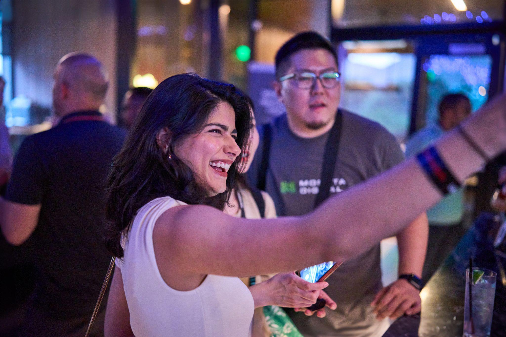 Woman laughing with her arm outstretched at an evening social event — Team offsite photography, Austin A woman laughing with her arm outstretched at an evening social event