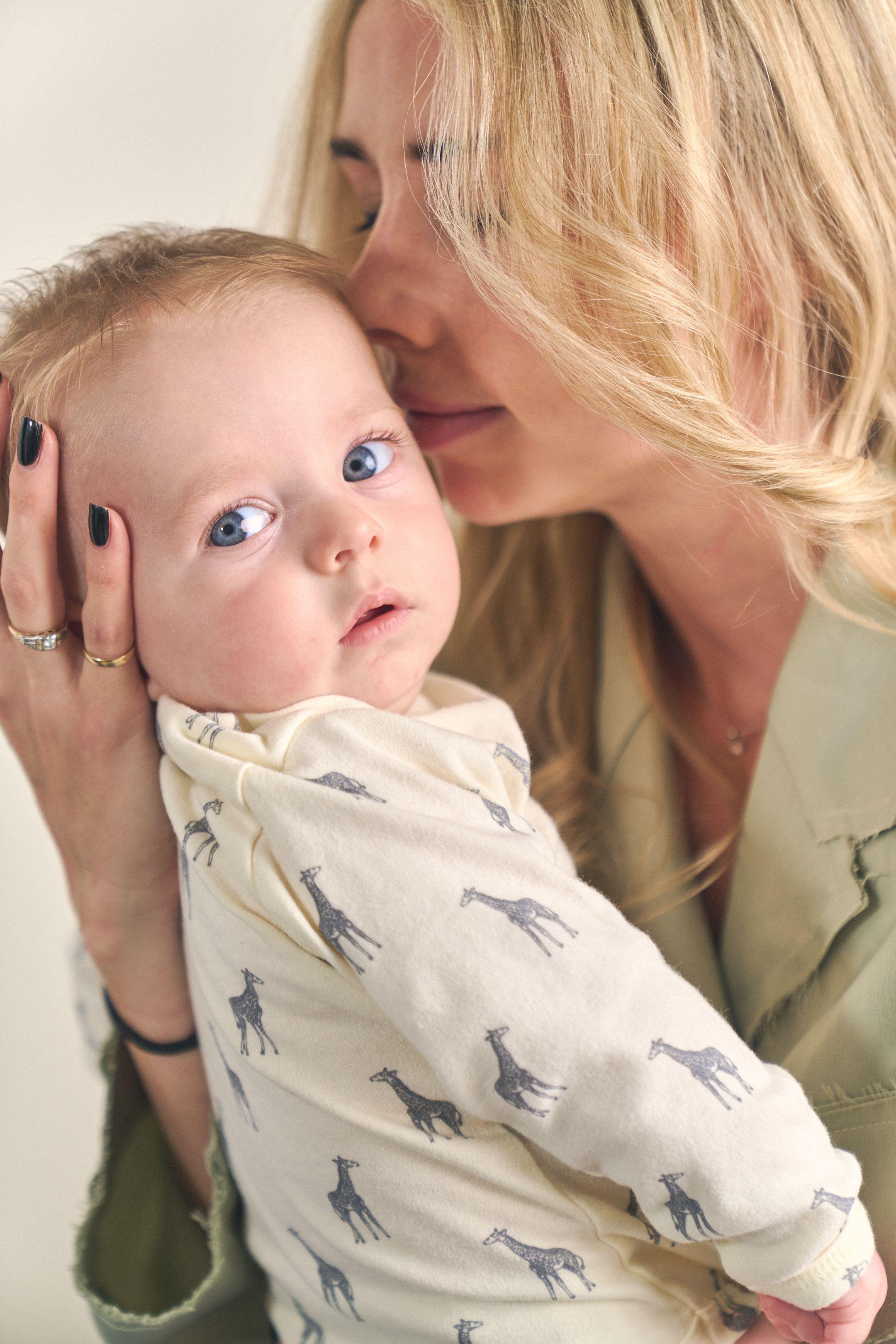 Mother kissing her baby's head as the baby looks toward the camera — Newborn photography, Austin A mother kissing her baby's head as the baby looks toward the camera.