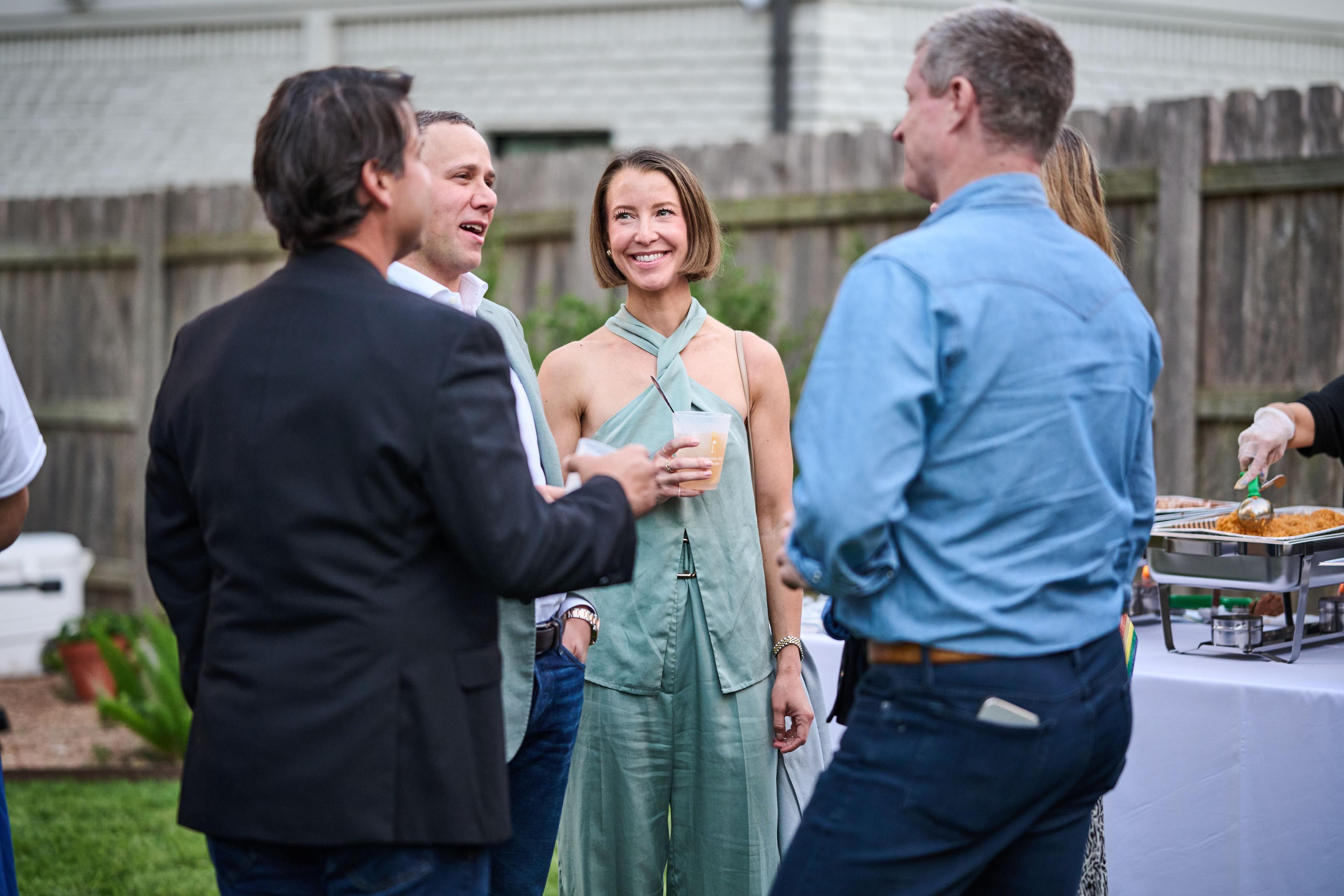 Guests in conversation on a patio, one woman in a pale green jumpsuit laughing — Formal Celebrations photography, Austin Guests in conversation on a patio, one woman in a pale green jumpsuit laughing.