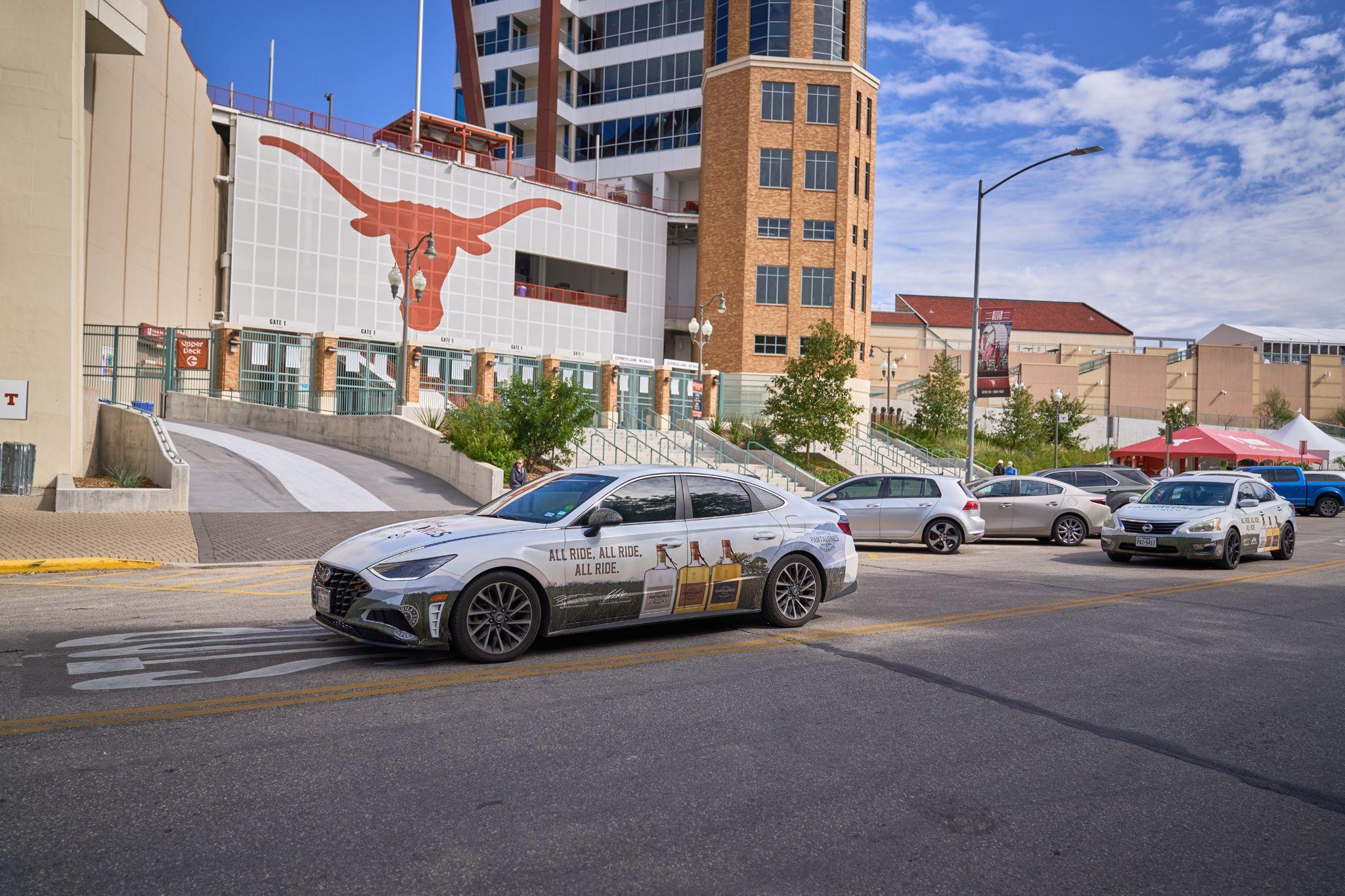 White car parked on a downtown street below a building with a large longhorn logo — Downtown Austin photography, Austin A white car parked on a downtown street below a building with a large longhorn logo.