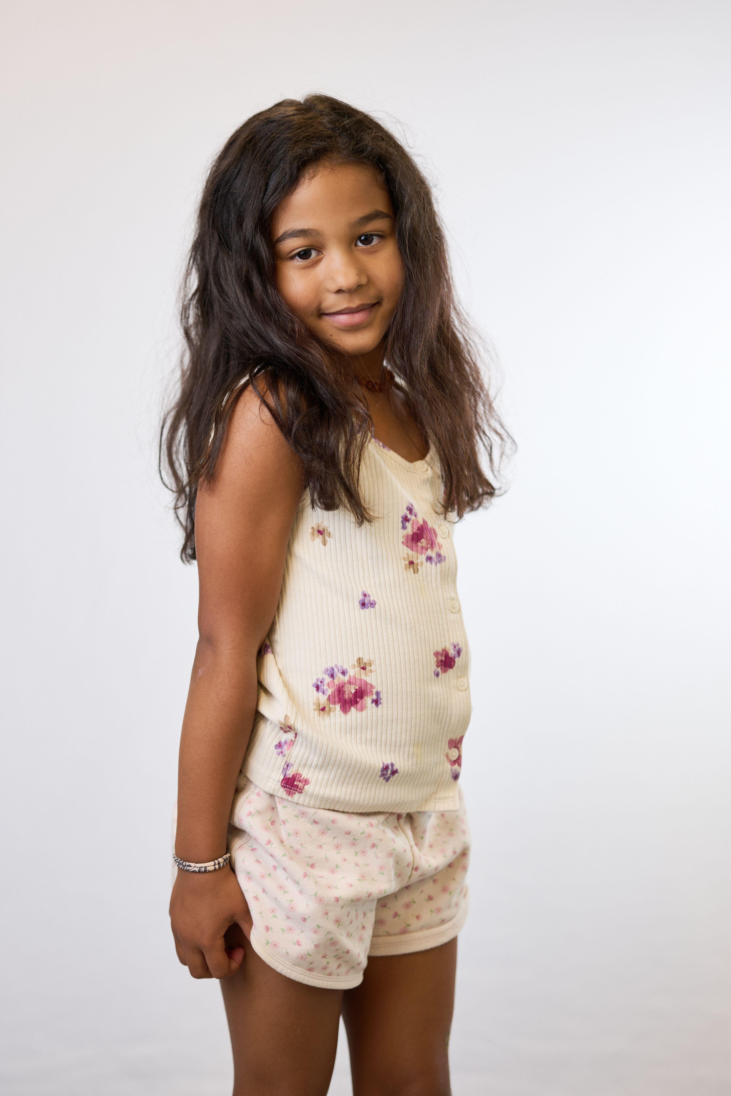 Girl in a floral romper looking over her shoulder on a plain light backdrop — Mobile photo studio, Austin A girl in a floral romper looking over her shoulder on a plain light backdrop