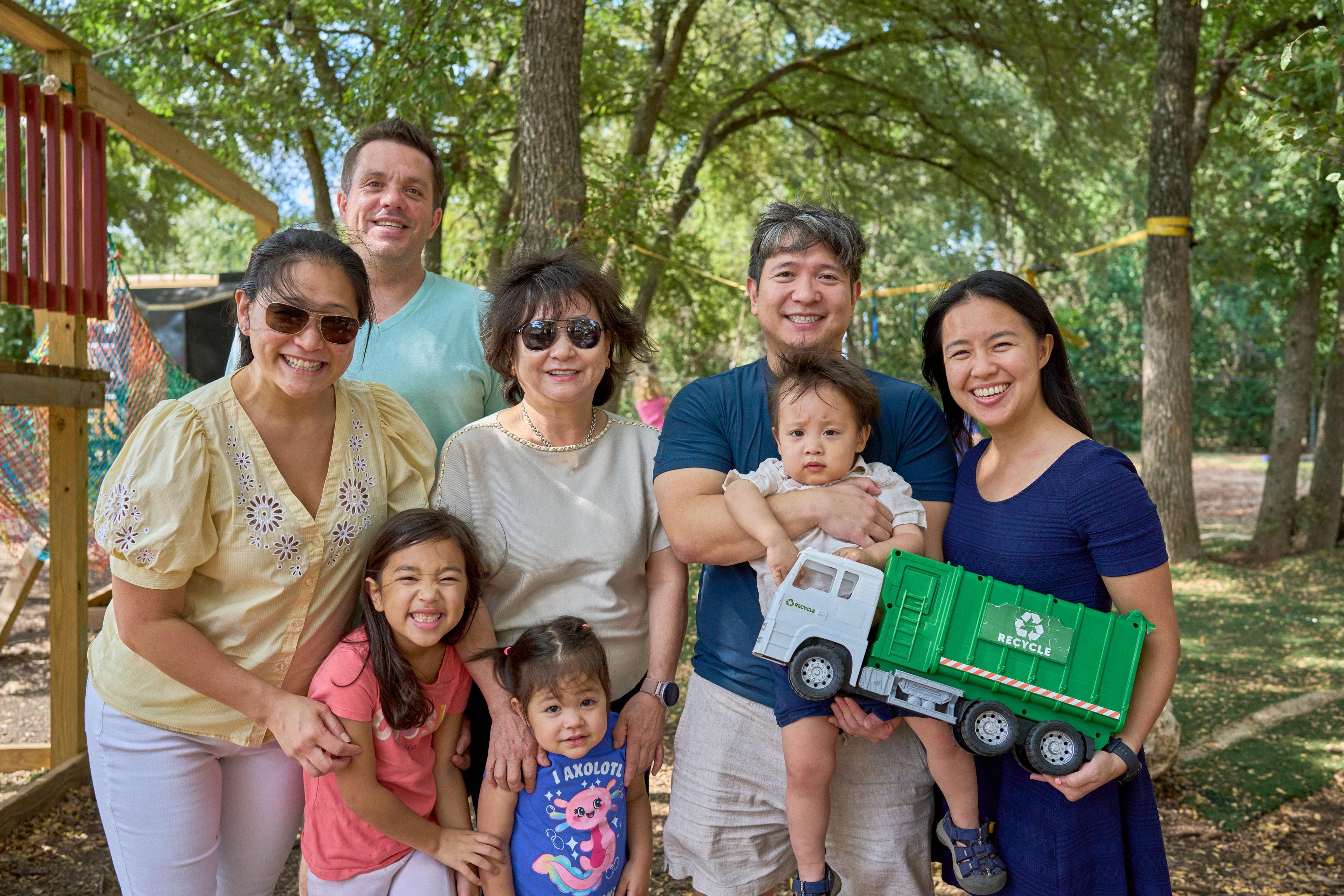 Three generations of a family posed together on a lawn, the toddler holding a toy truck — Family Parties photography, Austin Three generations of a family posed together on a lawn, the toddler holding a toy truck.