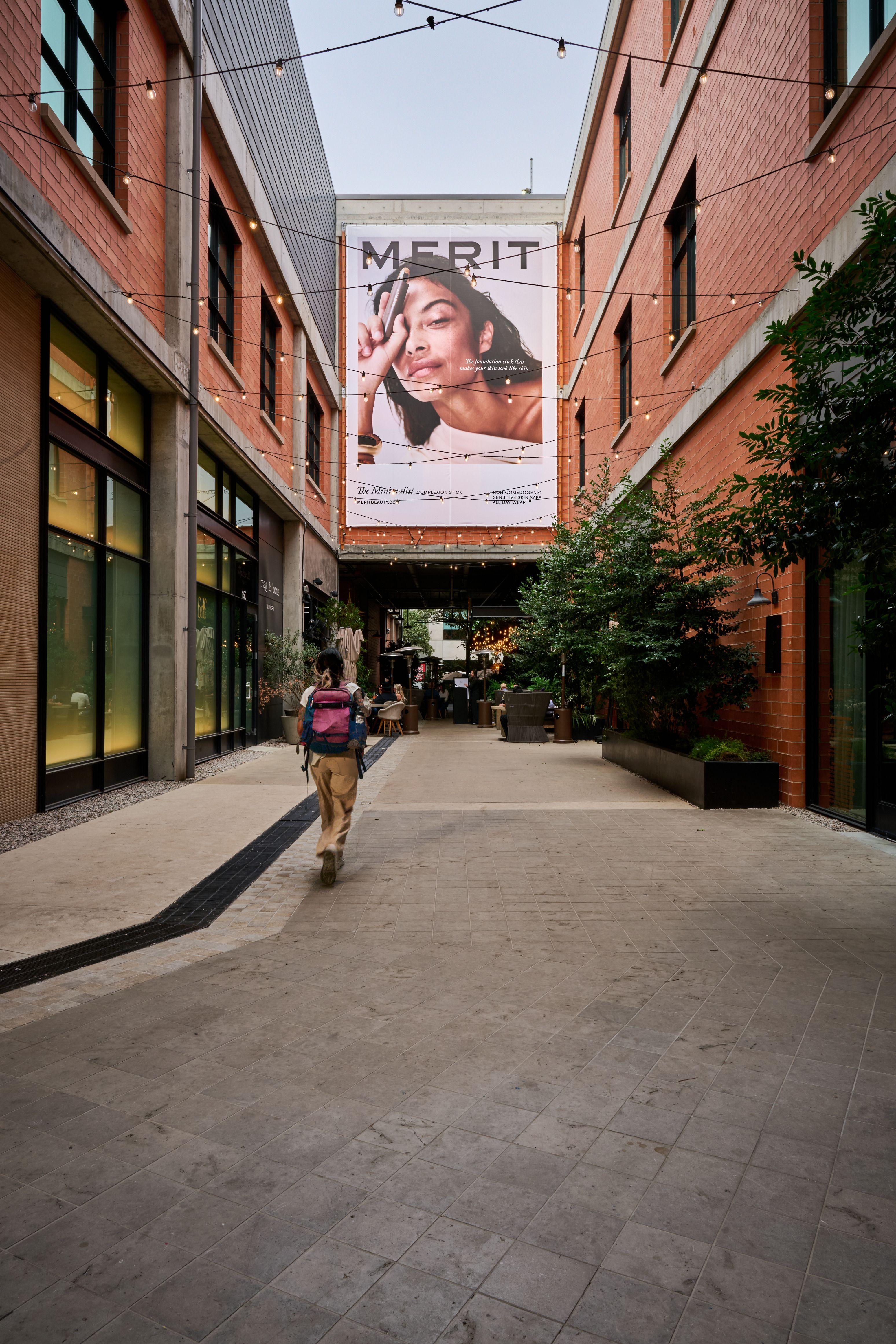Merit beauty campaign banner on a brick wall above a narrow shopping alley — Outdoor media photography, Austin A Merit beauty campaign banner on a brick wall above a narrow shopping alley.