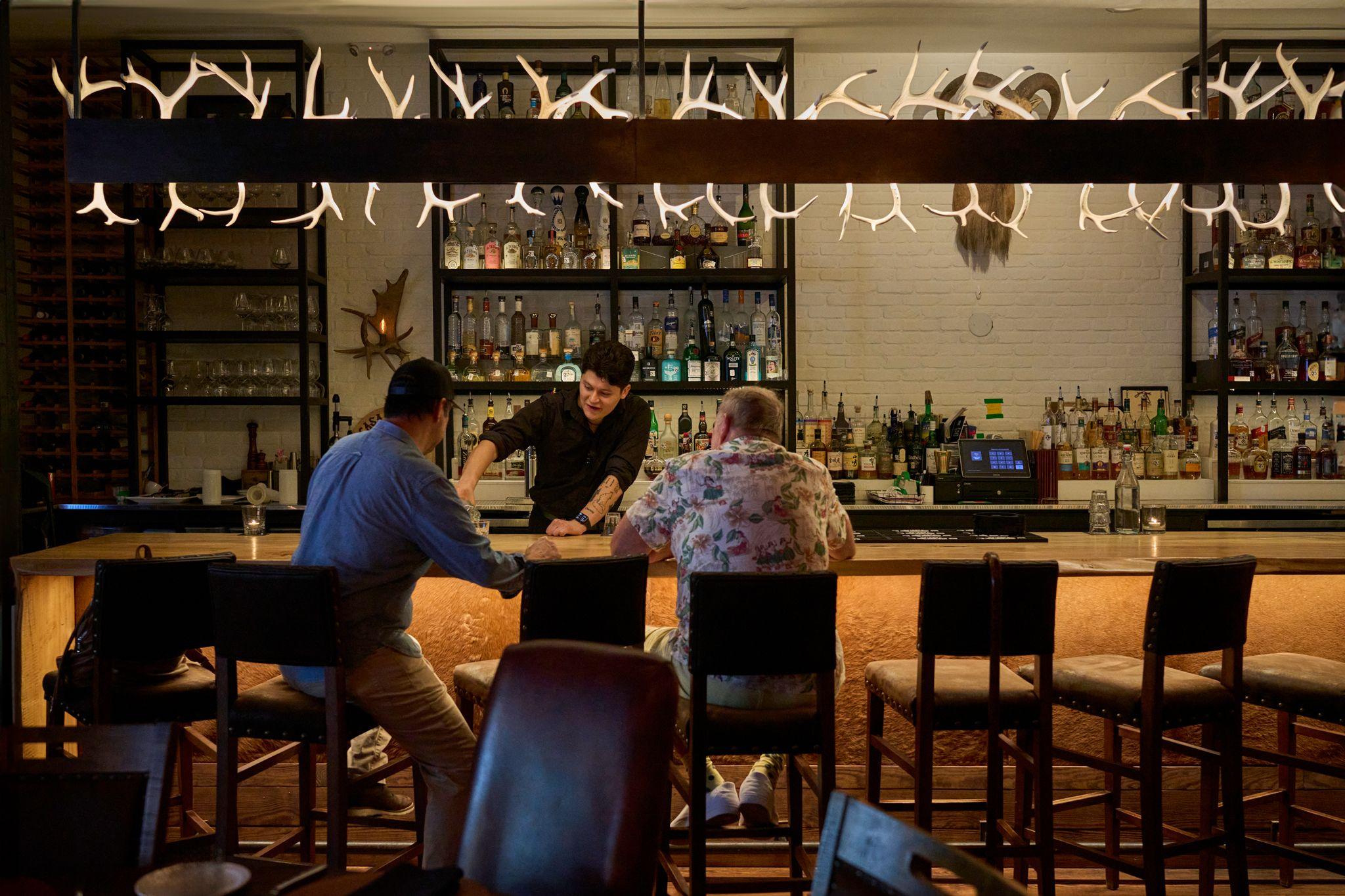 Guests seated along a long bar with a bartender working behind it — Hospitality & leisure photography, Austin Guests seated along a long bar with a bartender working behind it.