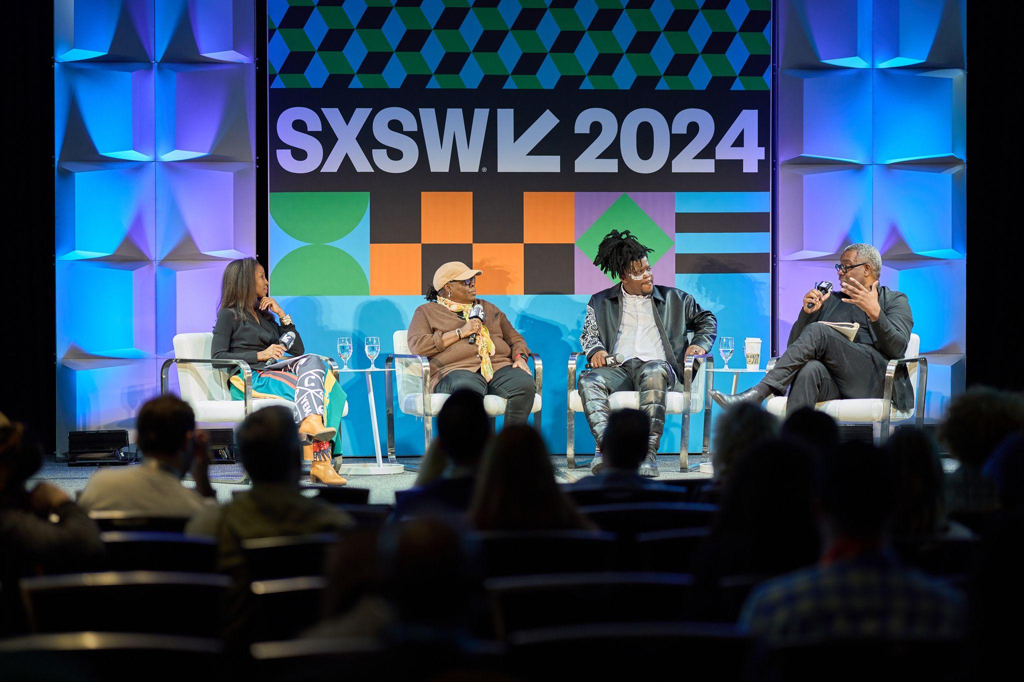 Panel seated on stage in front of a large geometric SXSW 2024 screen, audience silhouetted — Conventions & Tradeshows photography, Austin A panel seated on stage in front of a large geometric SXSW 2024 screen, audience silhouetted in front.