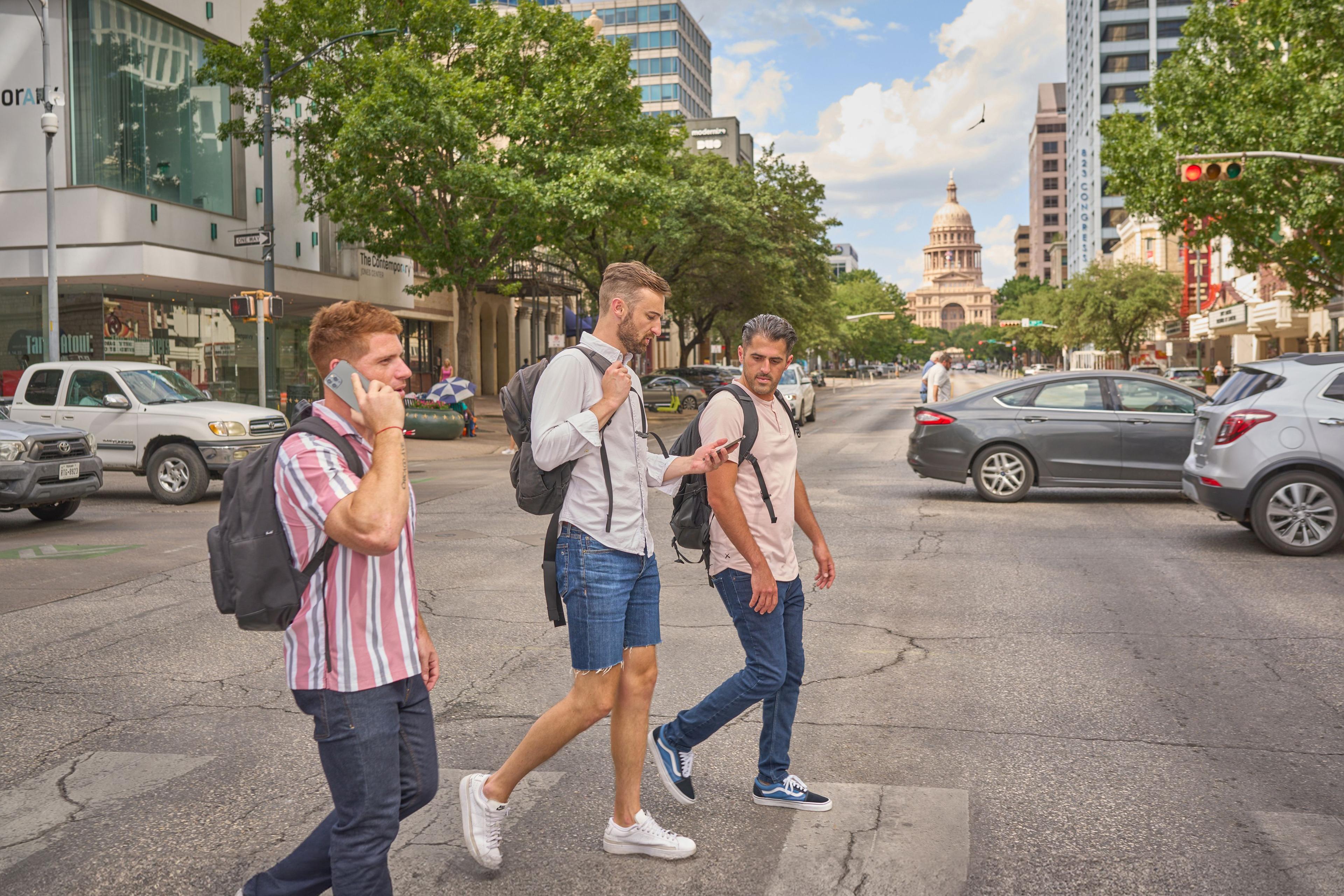 Three colleagues walking and talking on a street with the Texas Capitol in the distance — Team offsite photography, Austin Three colleagues walking and talking on a street with the Texas Capitol in the distance