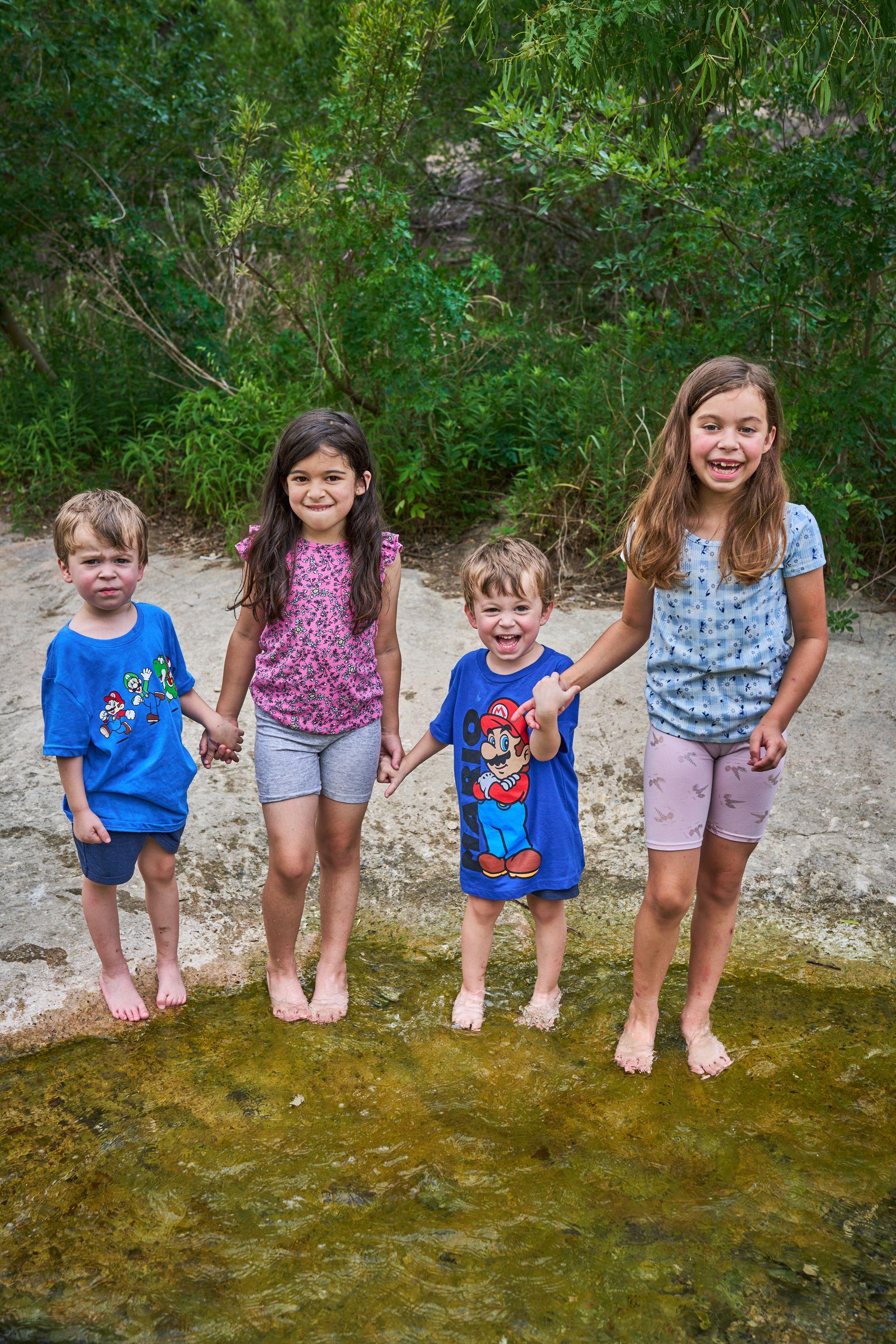 Four children standing barefoot in shallow creek water, holding hands — Bull Creek District Park photography, Austin Four children standing barefoot in shallow creek water, holding hands.
