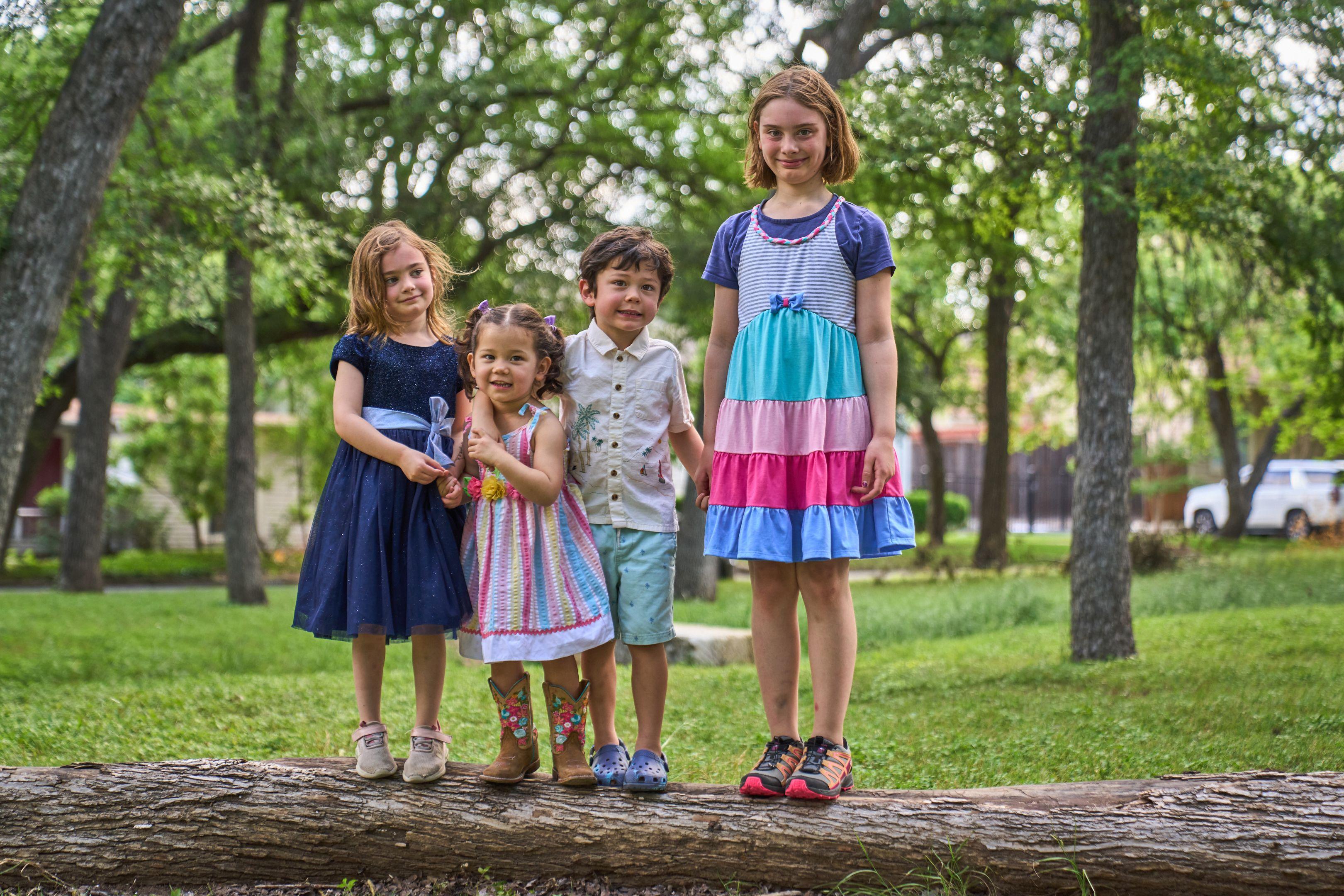 Four children standing along a fallen log in a park, tallest to smallest — Kids Portraits photography, Austin Four children standing along a fallen log in a park, tallest to smallest.