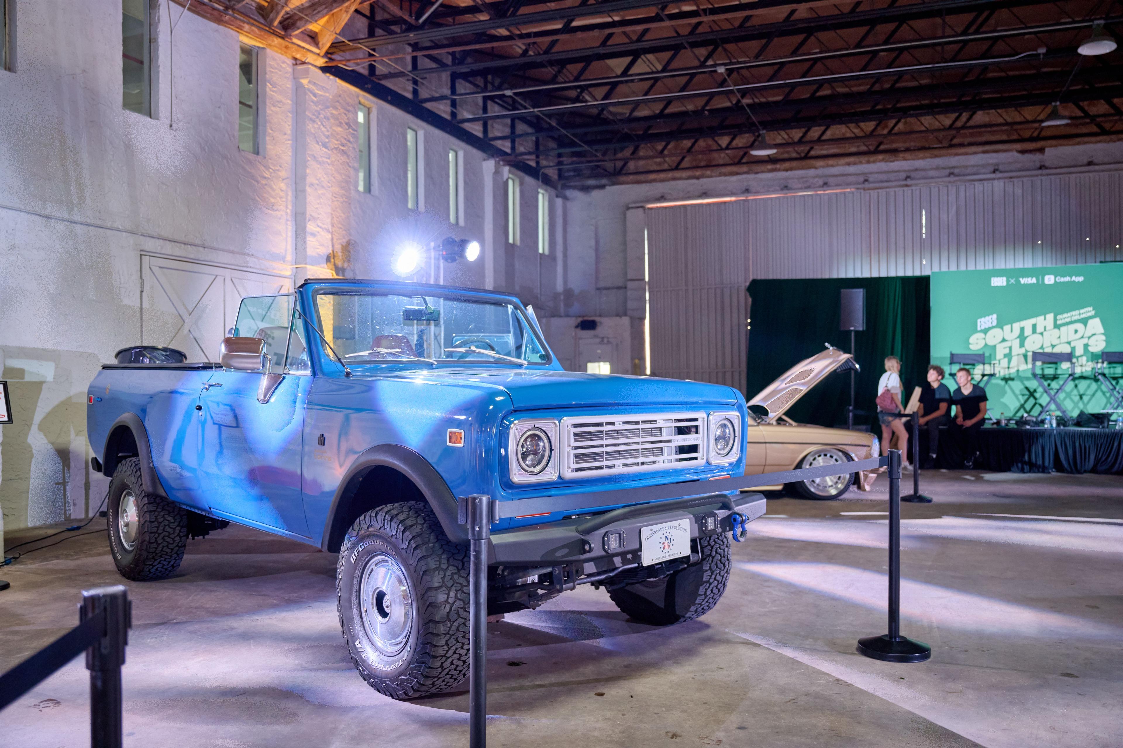 Restored blue Scout pickup spotlit inside a dark warehouse at a brand activation — Brand Collaborations photography, Austin A restored blue Scout pickup spotlit inside a dark warehouse at a brand activation.
