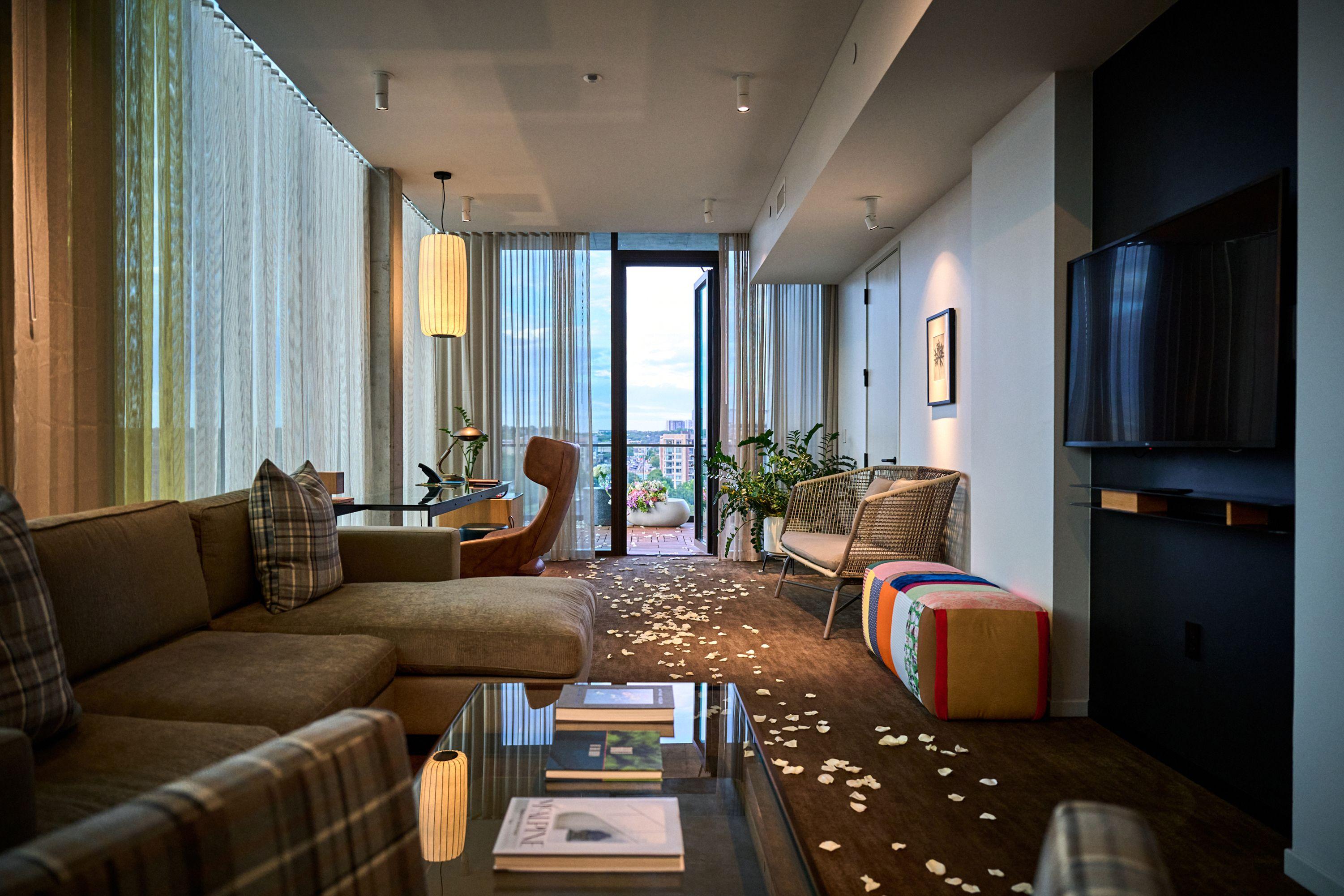 Hotel suite with lounge chairs, floor-to-ceiling windows and rose petals scattered — Hospitality & leisure photography, Austin A hotel suite with lounge chairs, floor-to-ceiling windows and rose petals scattered across the floor.