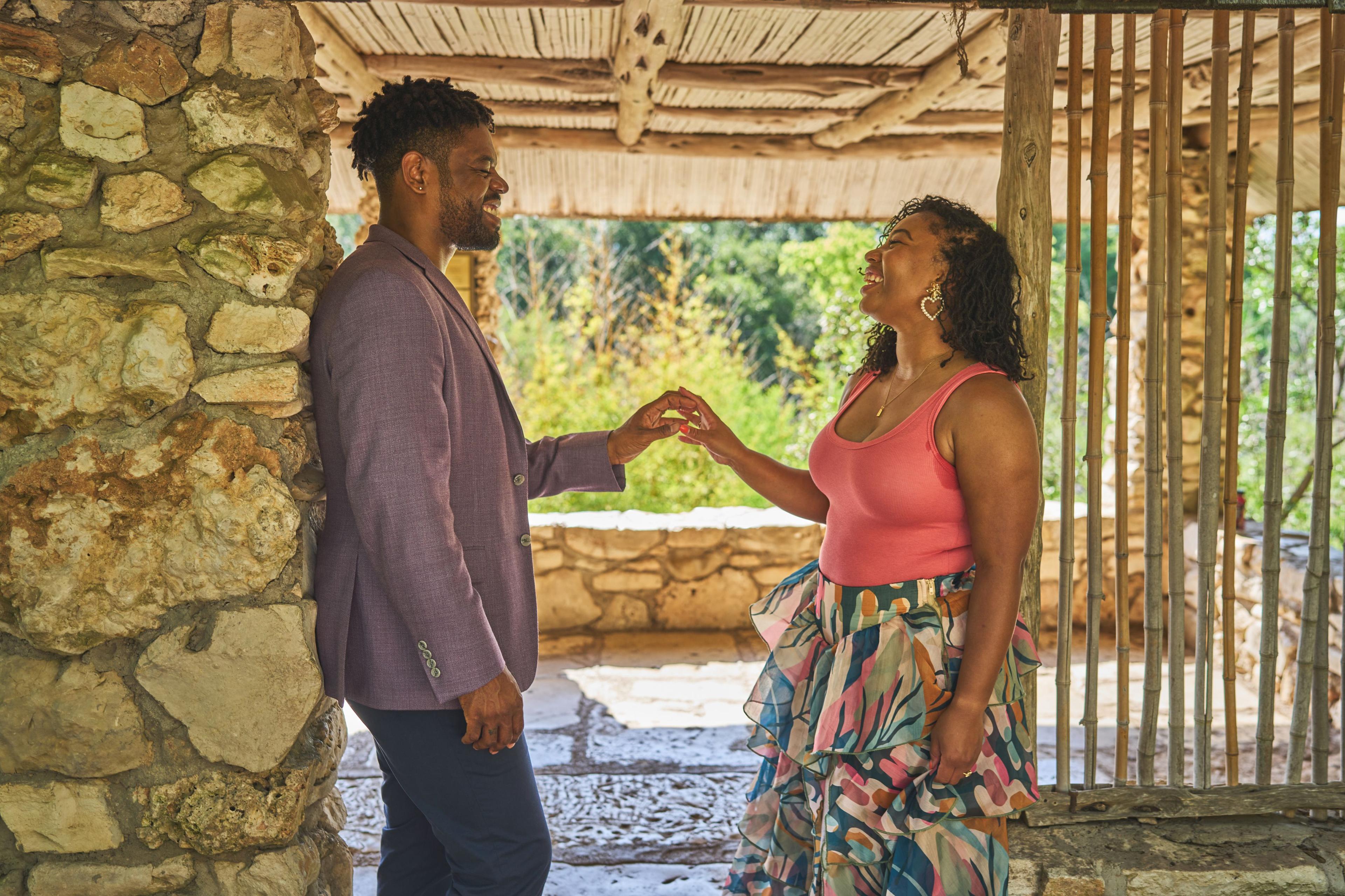 Couple reaching for each other's hands beneath the thatched garden shelter — Zilker Botanical Gardens photography, Austin A couple reaching for each other's hands beneath the thatched garden shelter