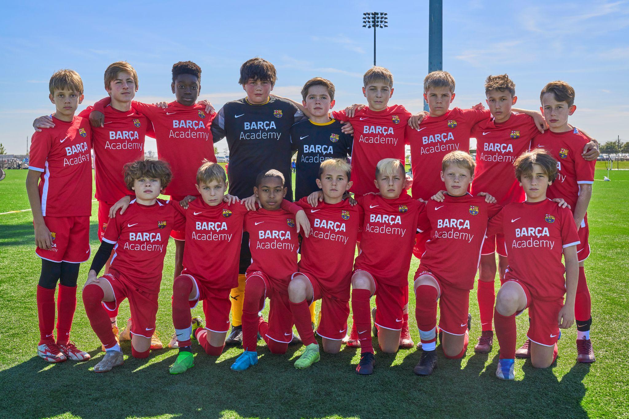 Youth football squad in red and navy Barça Academy kits posed in two rows on the pitch — Sports photography, Austin Youth football squad in red and navy Barça Academy kits posed in two rows on the pitch